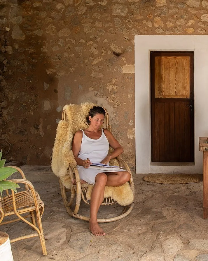 Marianne de Kuyper, coach and yoga teacher, reading in a rocking chair on a sunny stone terrace on Mallorca.