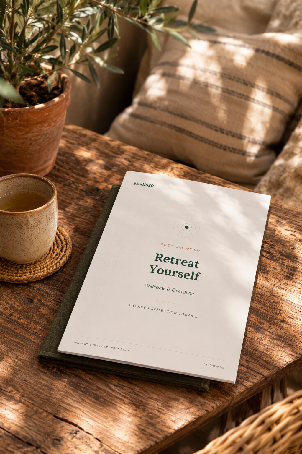 A4 printed copy of Retreat Yourself Book One: Welcome & Overview, a guided reflection journal by Studio20, resting on a notebook on a sunlit wooden table.