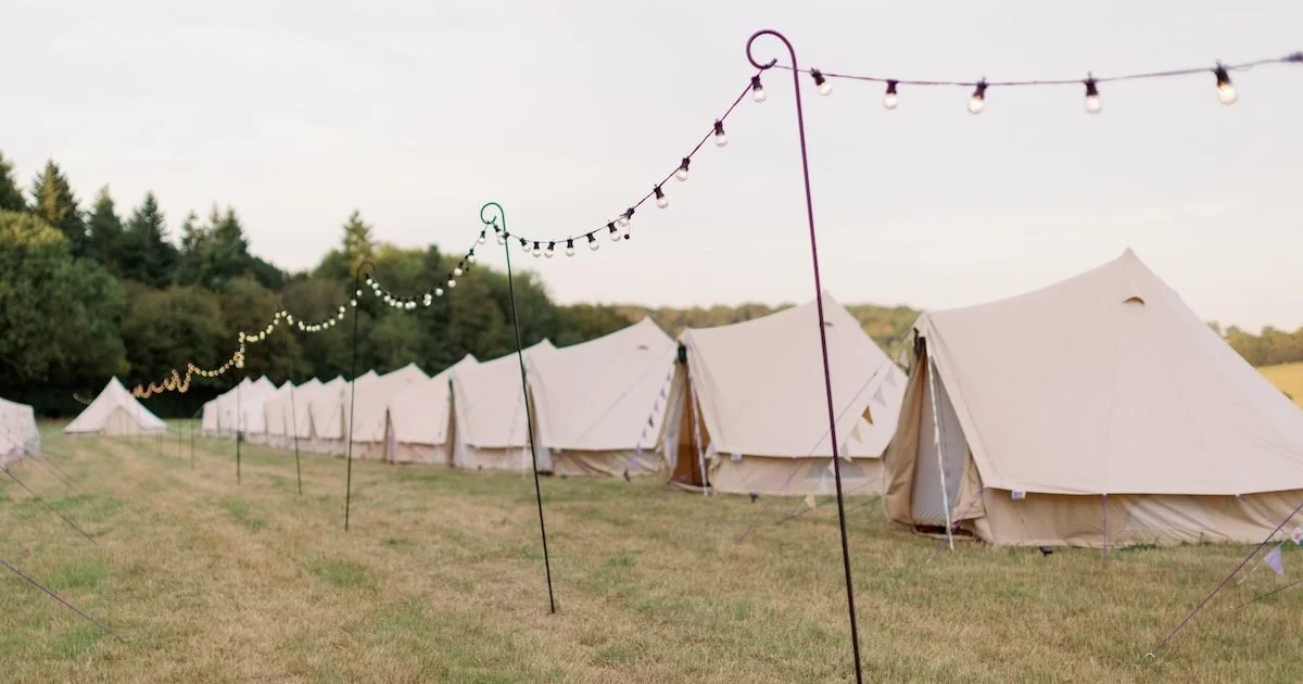 Bliss Cph - Glamping teltcamp med genrejsatte telte på en græsplæne, dekorationslamper hænger imellem lejrene