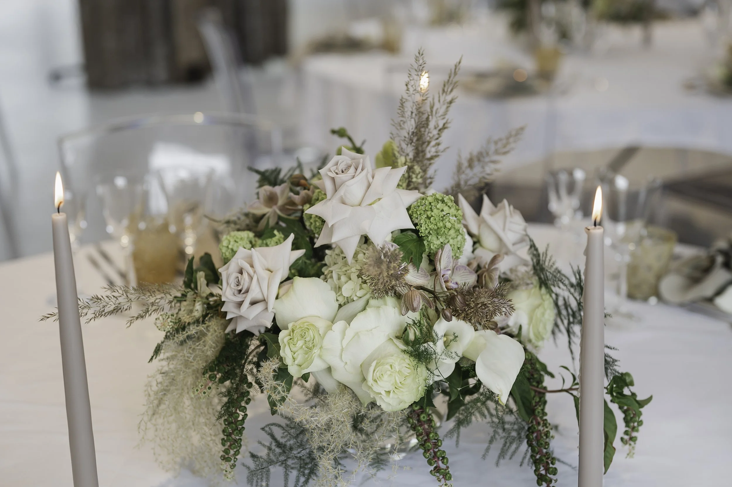 En elegant borddekoration med hvide og lyseblå blomster, omgivet af to hvide stearinlys