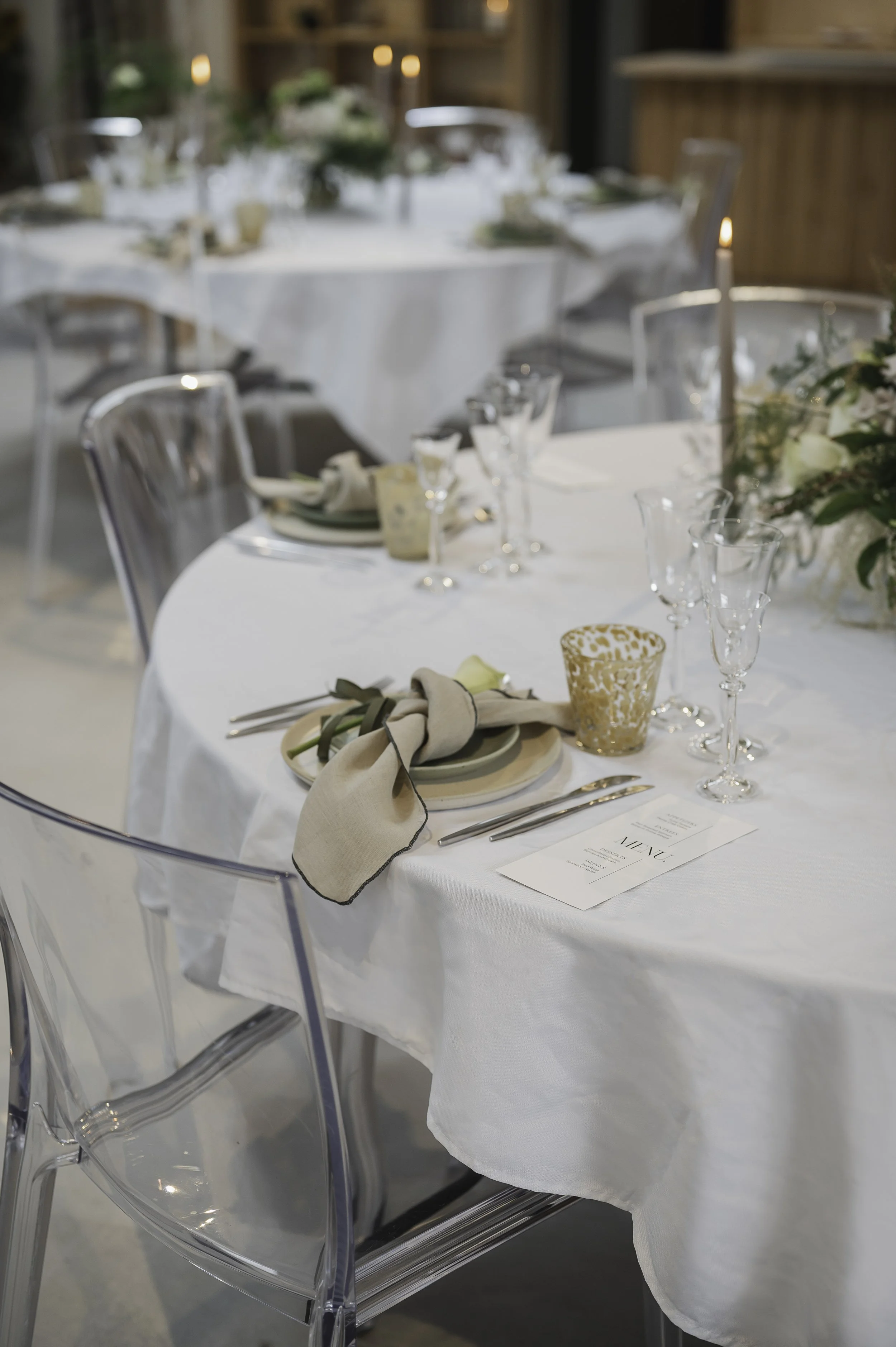 Festligt middagsbord med hvide duge, glas, tallerkener, bestik, servietter og blomsterdekorationer.