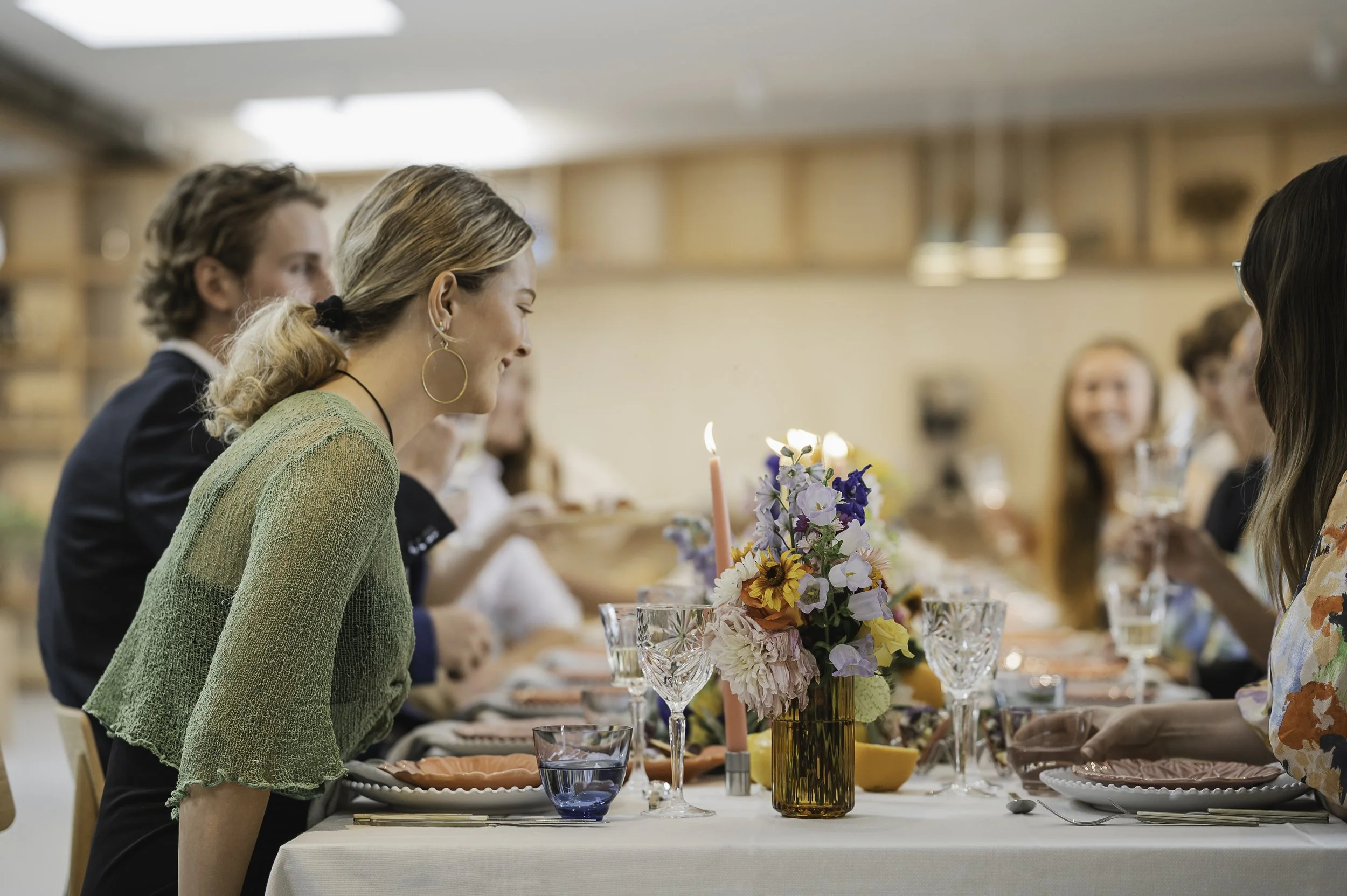 En bryllupsgruppe sidder ved en festlig borddækning med blomster, stearinlys og glas.