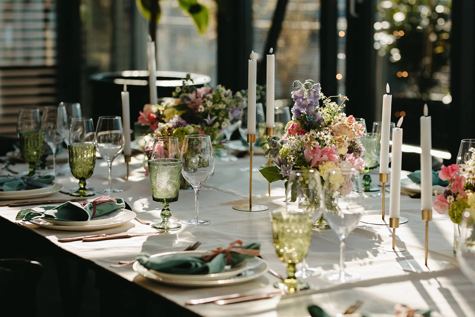 Elegant middagsbord dækket med blomsterdekorationer, stearinlys og glas i sollys.