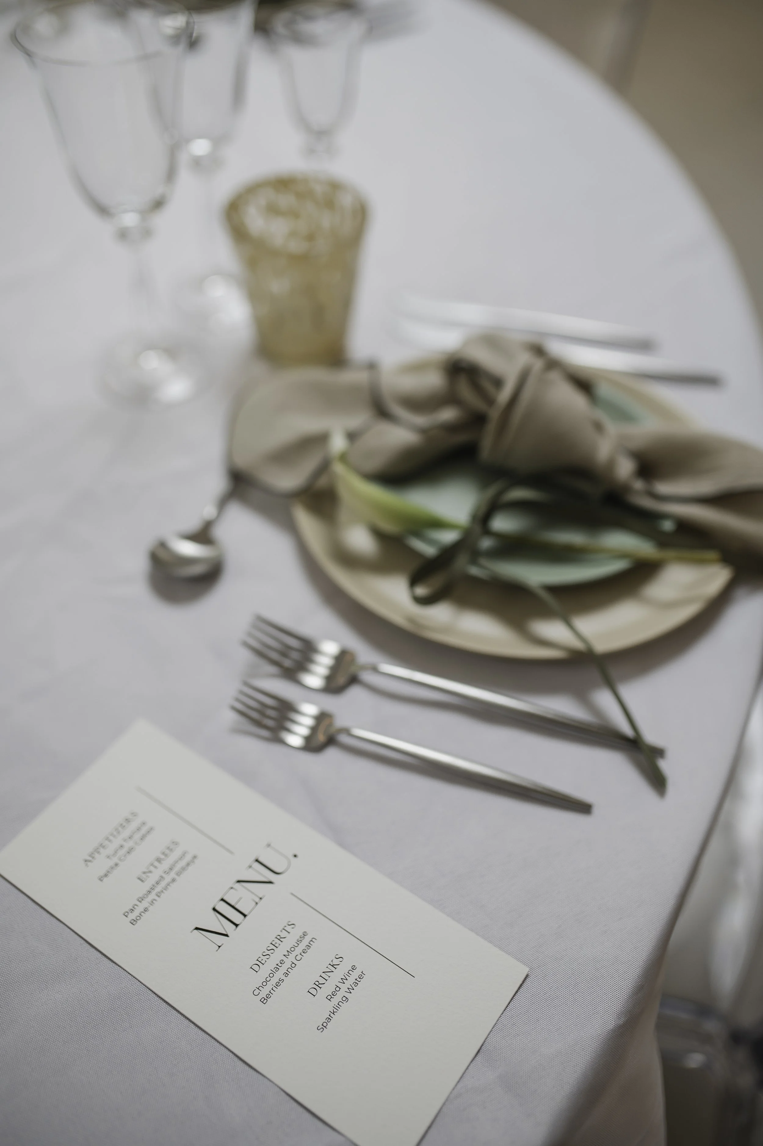 Bliss CPH – Borddækning med glassere, mat Sølvbestik fra Cutipol, en elegant menu, en tallerken fra Bornholms Keramikfabrik med en grøn serviet og en blomst