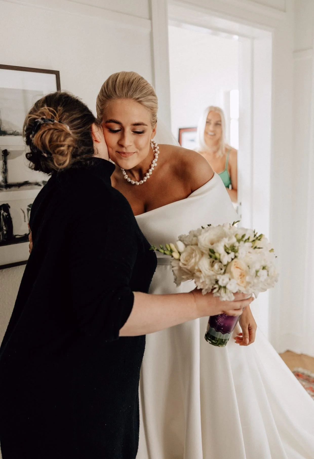 En brud krammer bryllupsplanlæggerens Cat Bjørnholt, mens en kvinde i baggrunden smiler.