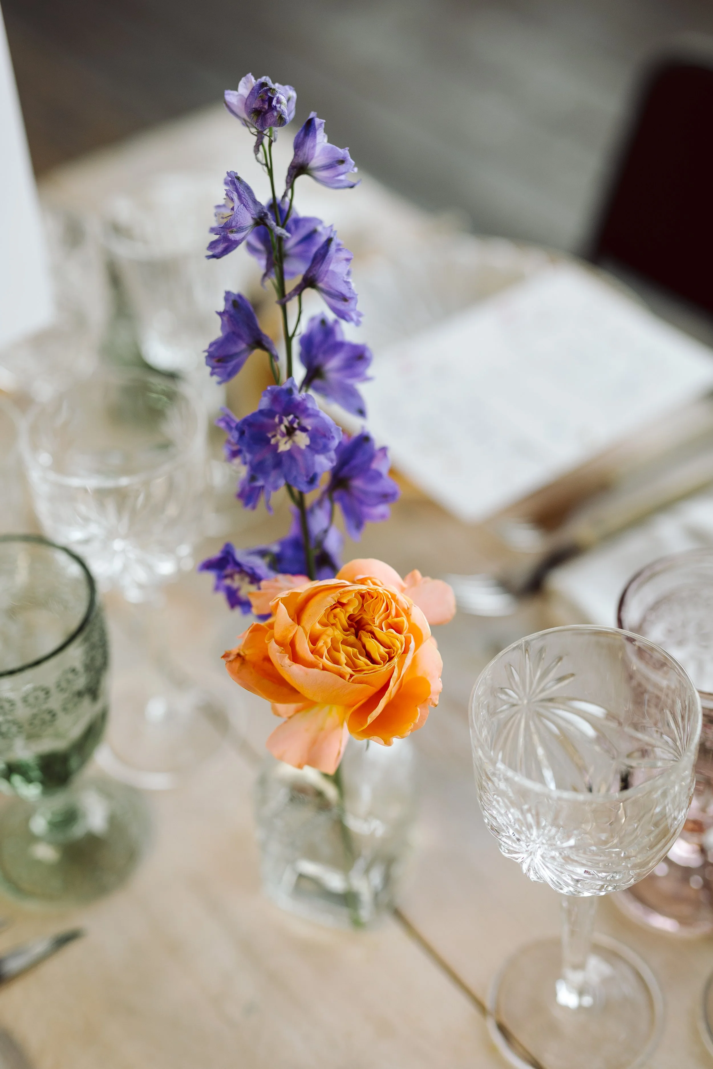 To blomster i en lille glasvase, en blå lilje og en orange rose af Bliss Cph