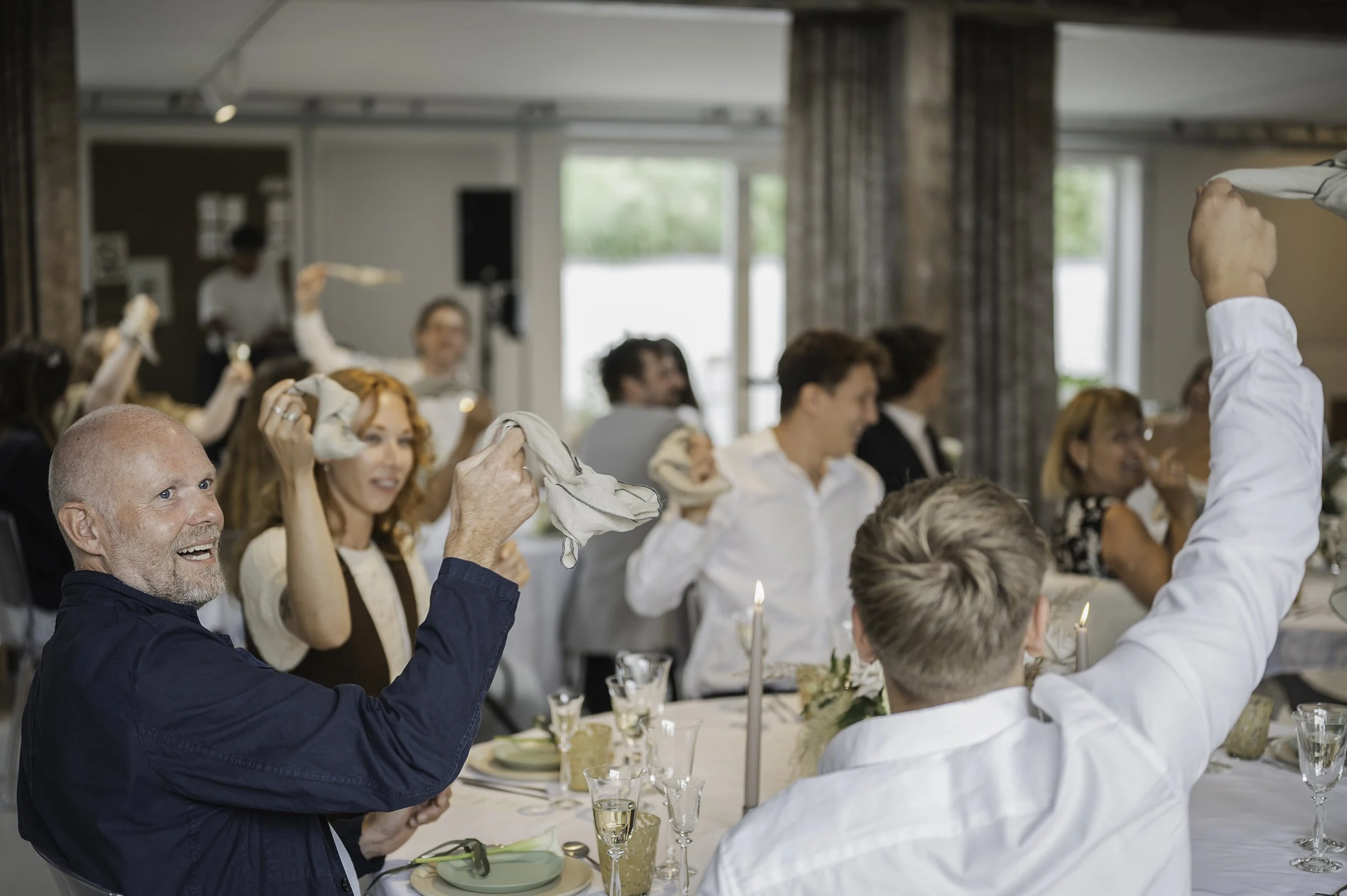 Gæster til et middagsarrangement, der vifter med servietter og smiler, i en elegant indrettet spisestue.