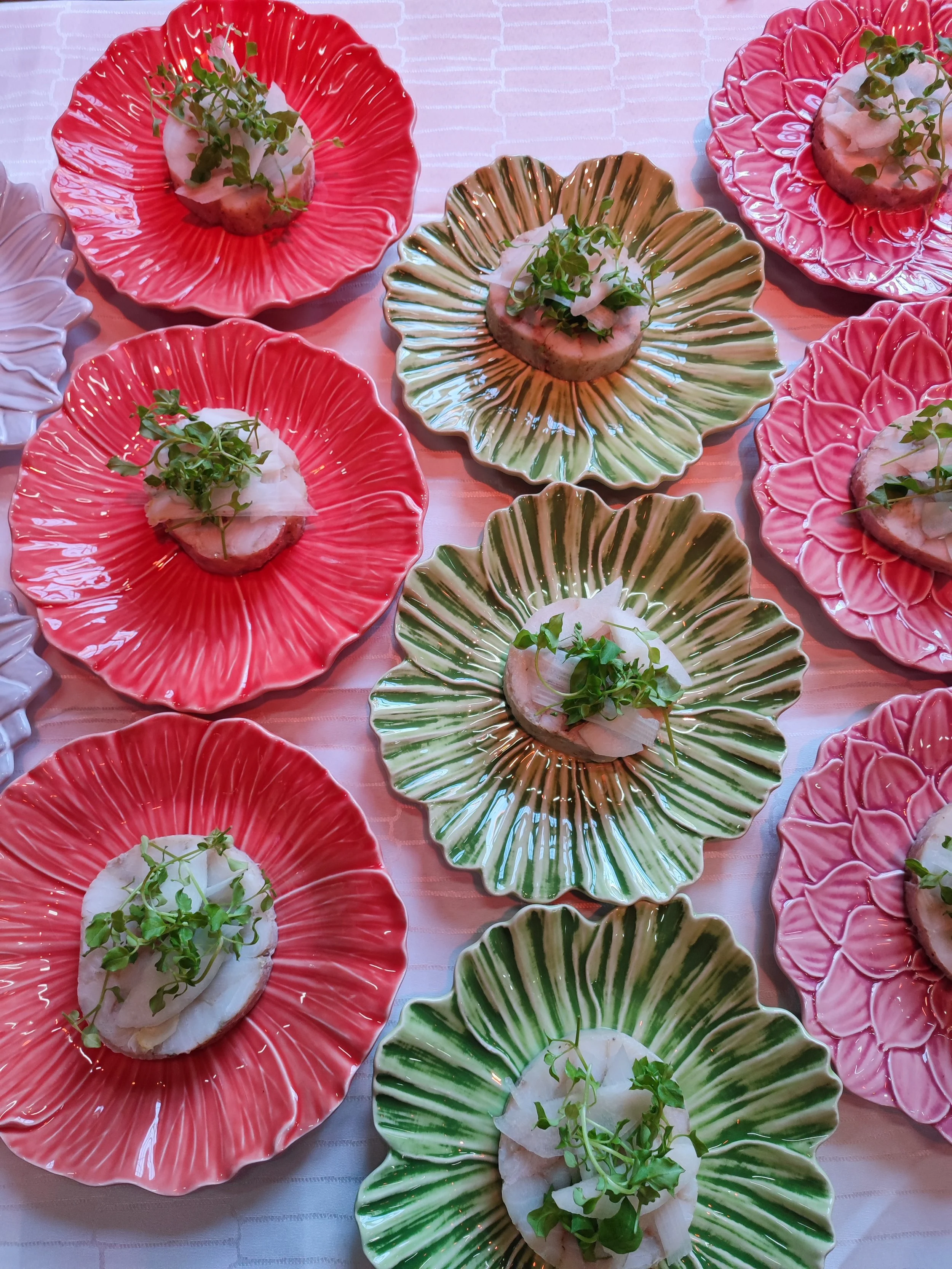 Små anretningsboller med en skive fisk, garniture og microgrønt, serveret på farverige, ruffled porcelænsfade i rød, grøn og pink.