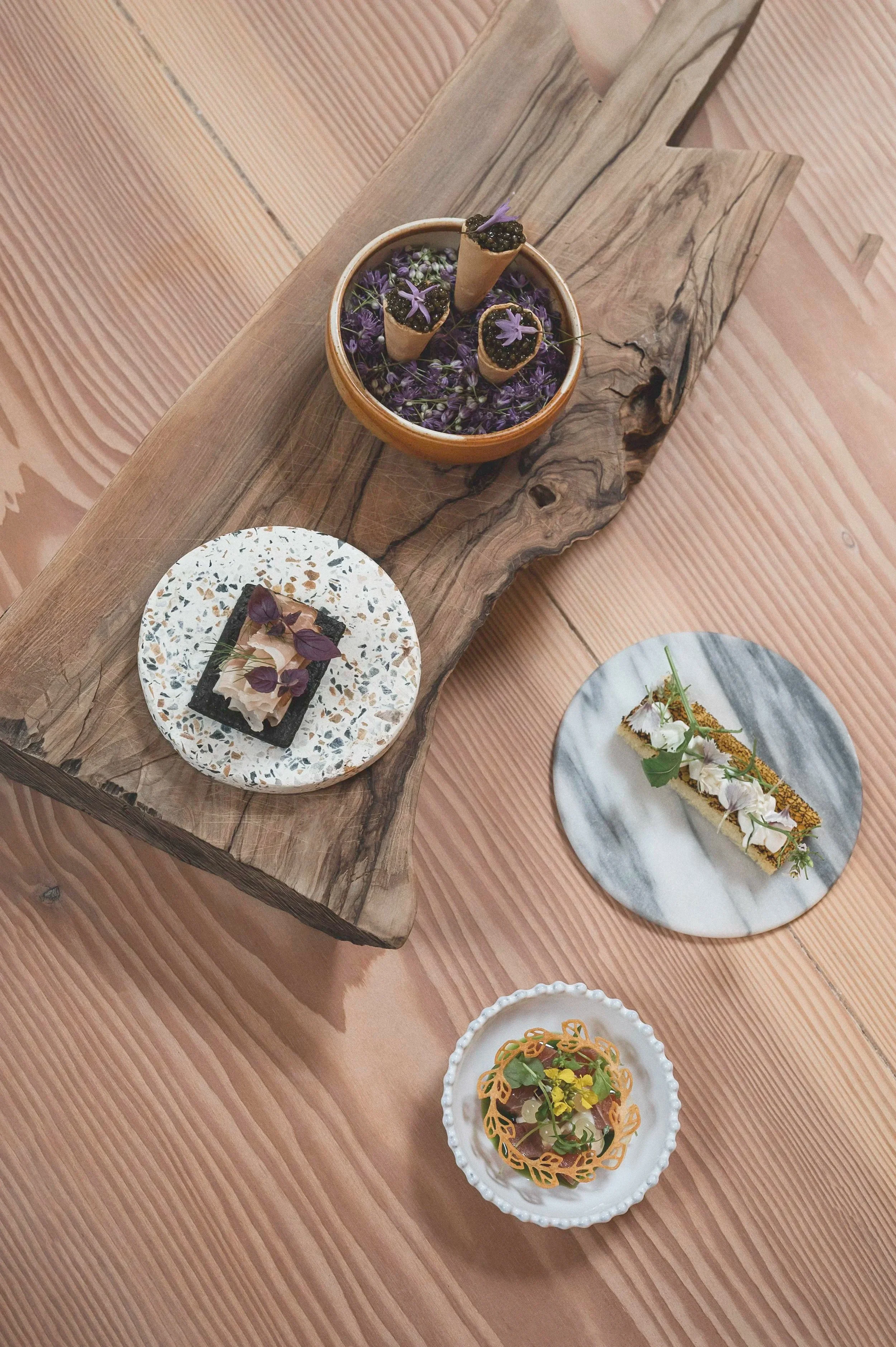 Bliss Cph - Elegante middagsretter lavet af Gas.op på danske designertallerkener, inklusive en tærte med blomster, en spiselig blomsterskulptur og mørt kød med pynt, udstillet på en træplade.