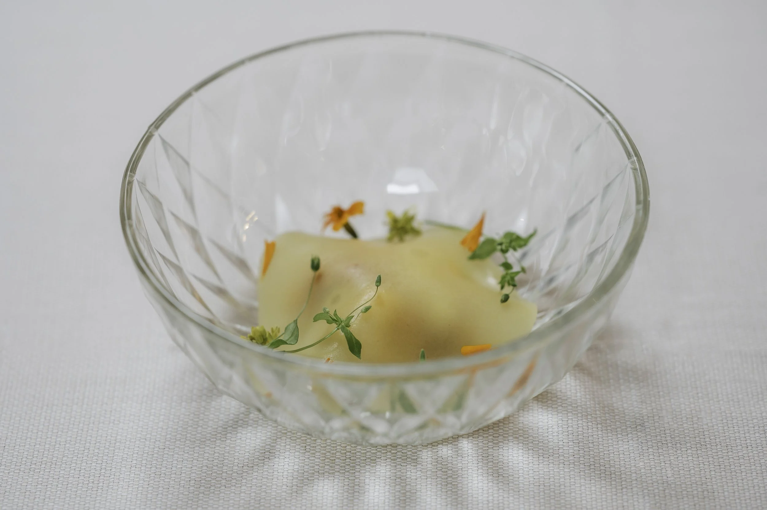 En glas skål med en klat smør pyntet med små frø, urter og gulerodsstykker.