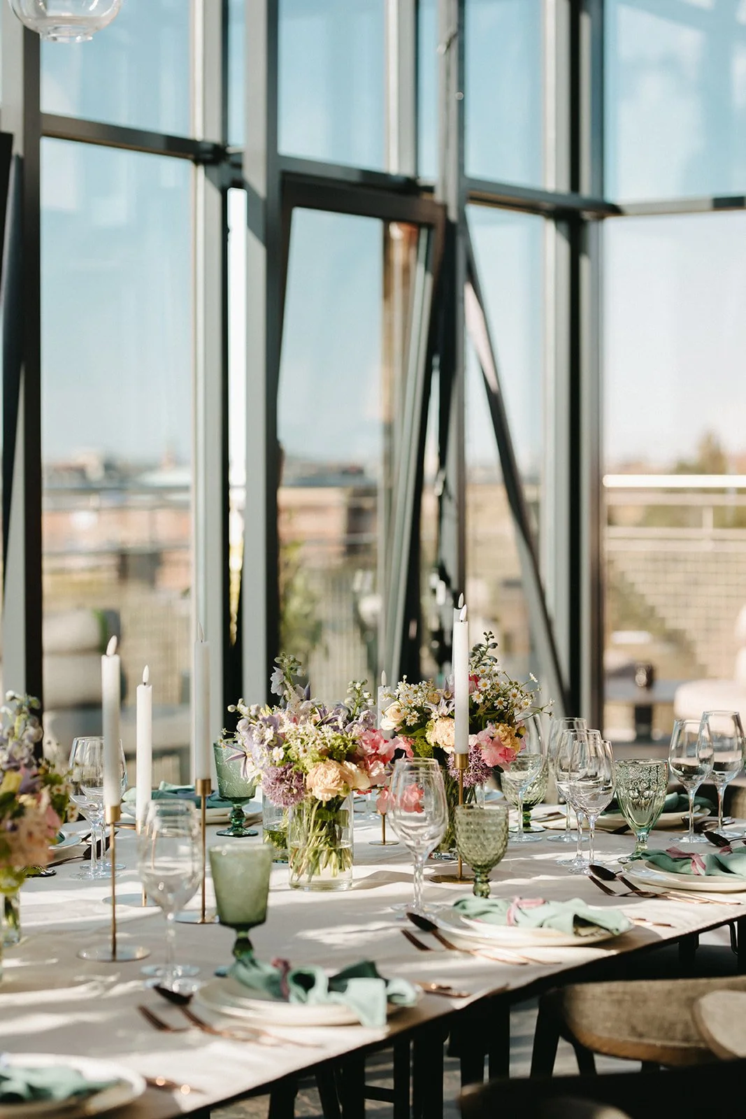 Festbord med blomsterdekorationer, stearinlys og glas i et modernt, lyst rum med store vinduer.