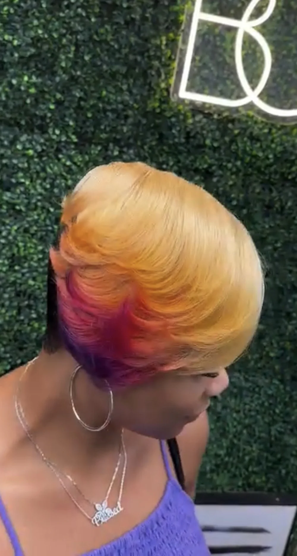 Client with a bold copper and violet cut in front of the salon's neon BOSS sign