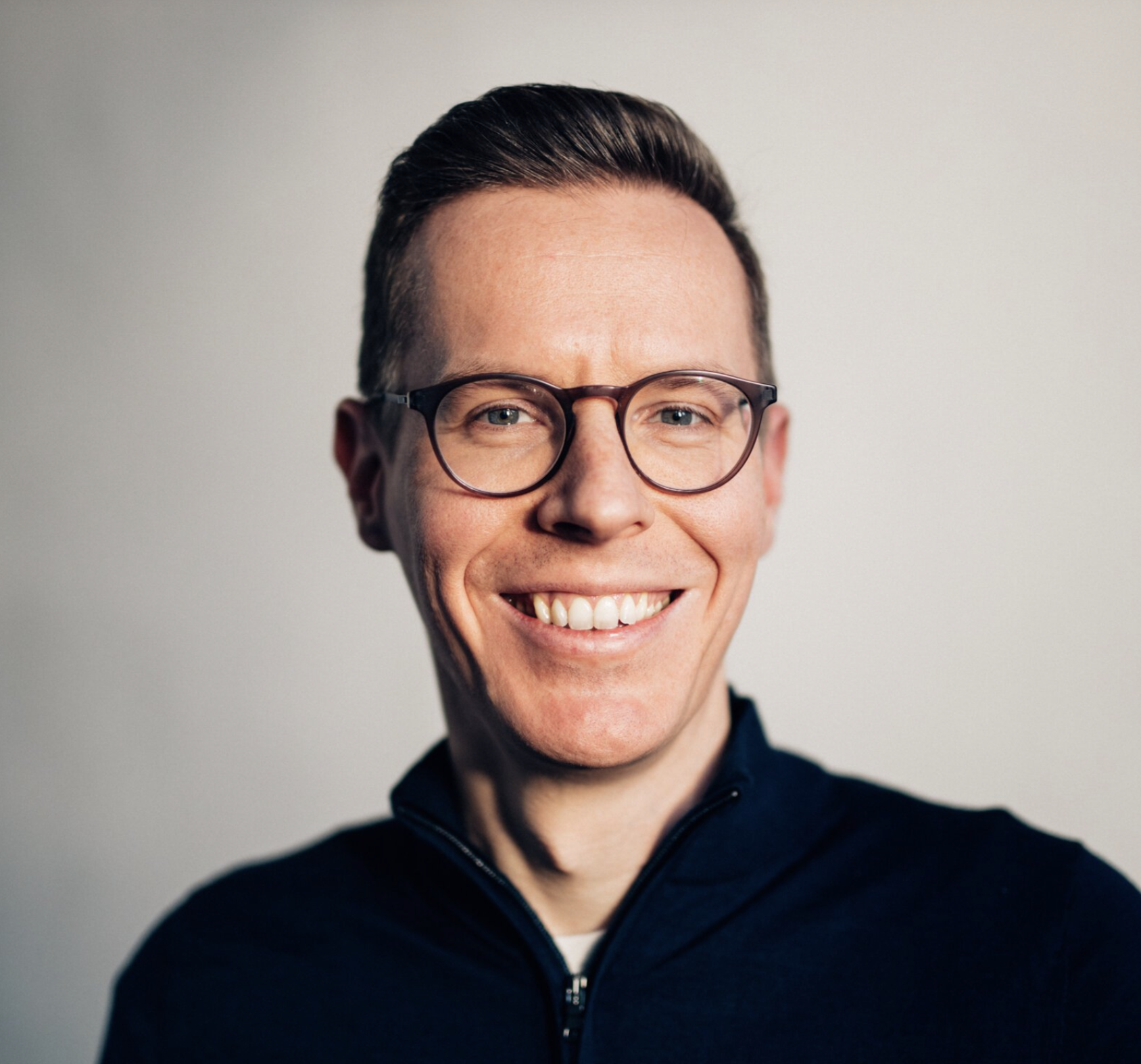 Porträt von Stefan Krumnow, eines lachenden Mannes mit Brille vor hellem Hintergrund.