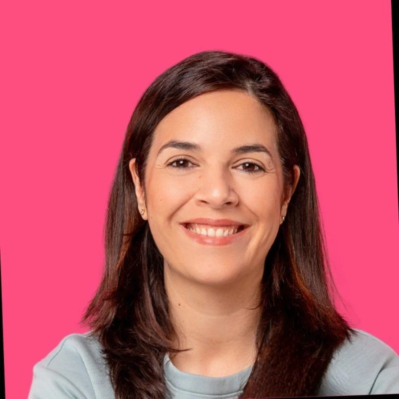 Nahaufnahme einer lächelnden Frau mit braunen Haaren vor pinkem Hintergrund.