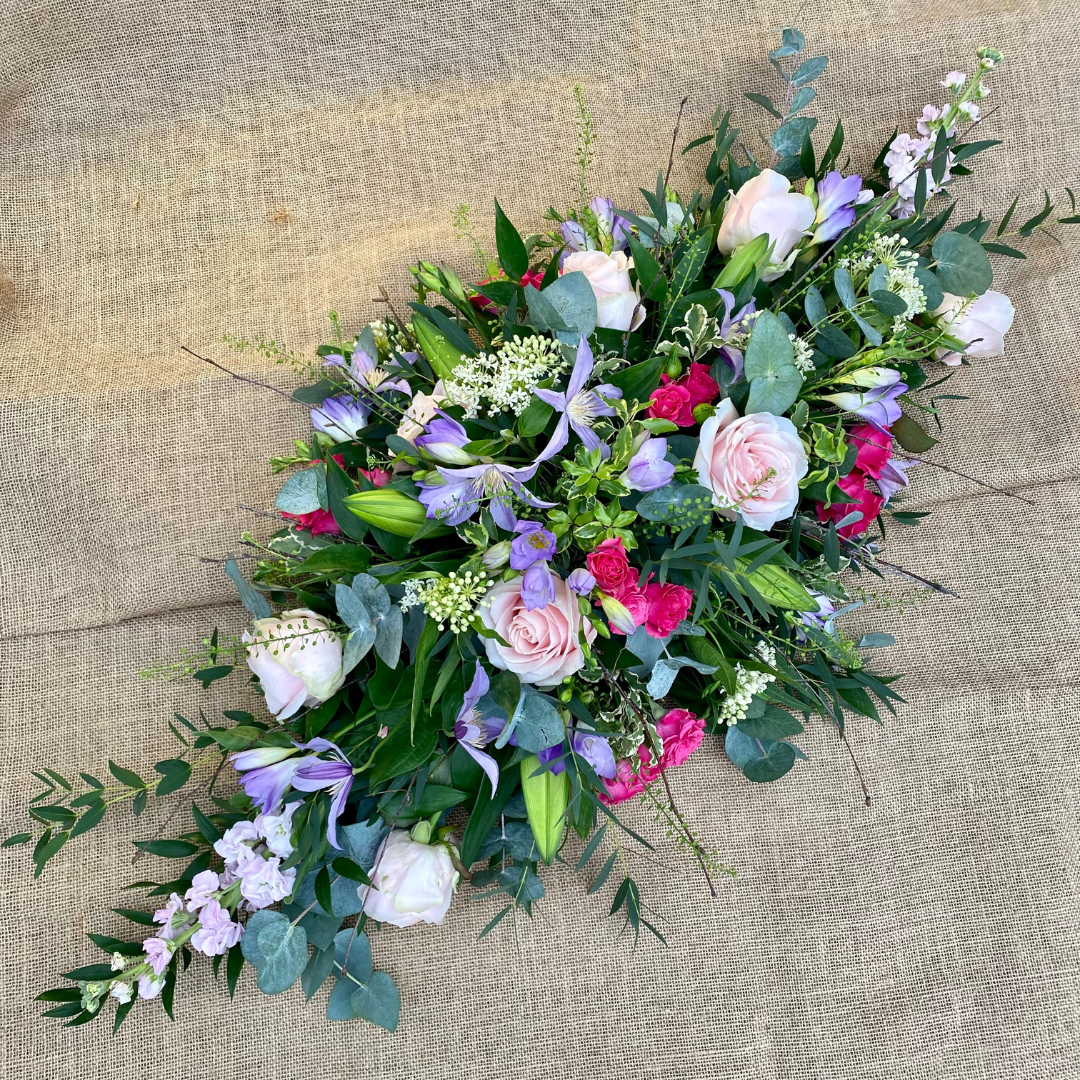 Coffin spray 3 ft long tapered design made with pinks and purples including roses, lillies and freesias
