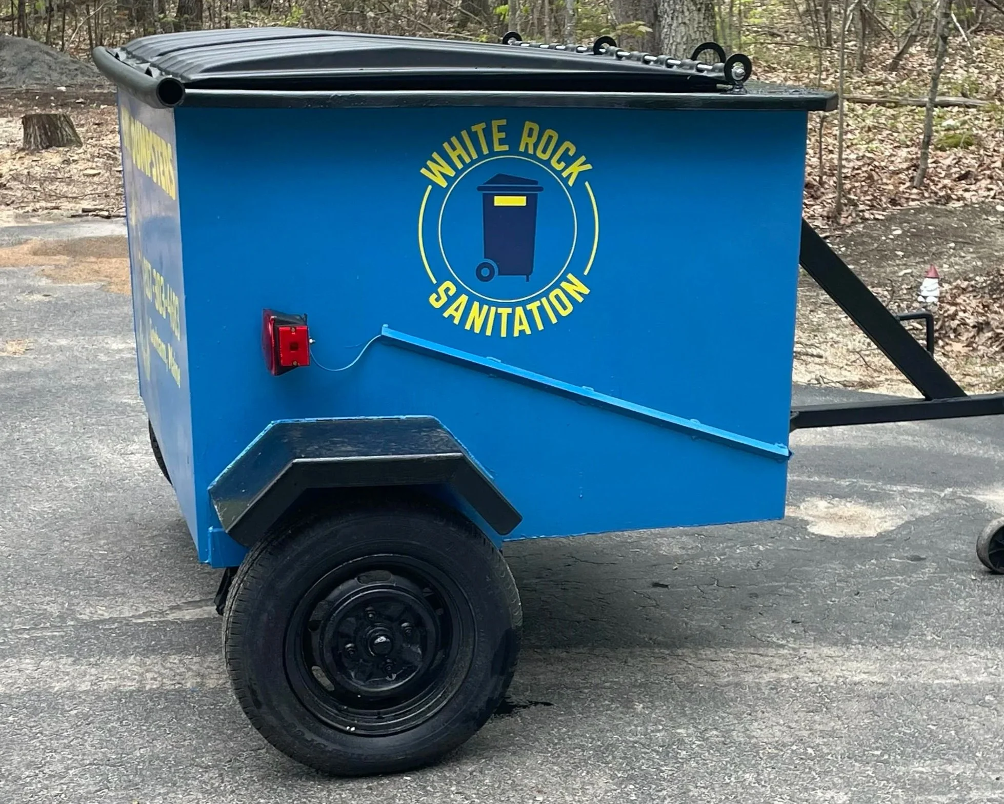 Blue sanitation cart with Yellow and blue logo reading 'White Rock Sanitation' and a trash can icon, parked on asphalt for White Rock Sanitation in Gorham, Maine.