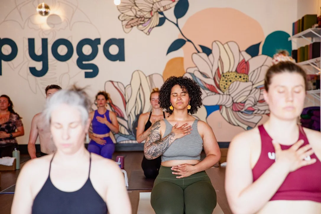 People practicing yoga in a studio with a large floral mural wall and the word 'yoga' written on it.