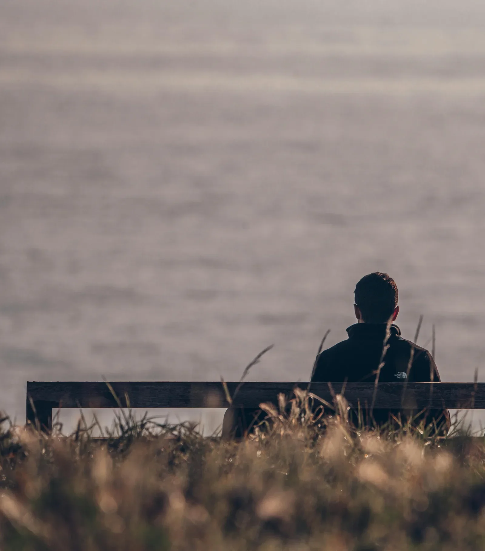 Man sitting alone on a bench overlooking the water, processing the grief and loneliness that can follow divorce