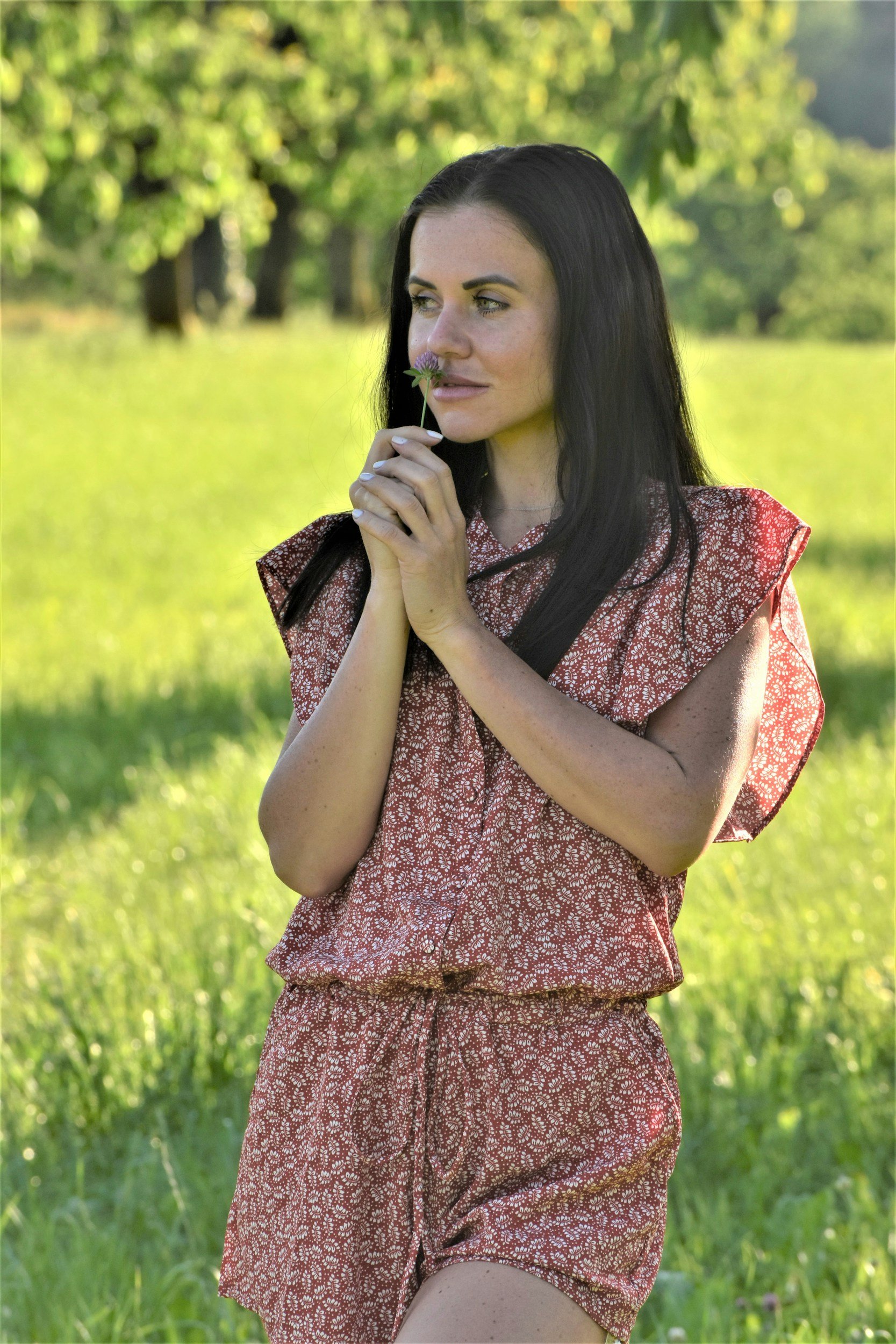Woman standing in nature holding a flower, representing emotional healing, nervous system regulation, and finding calm through therapy