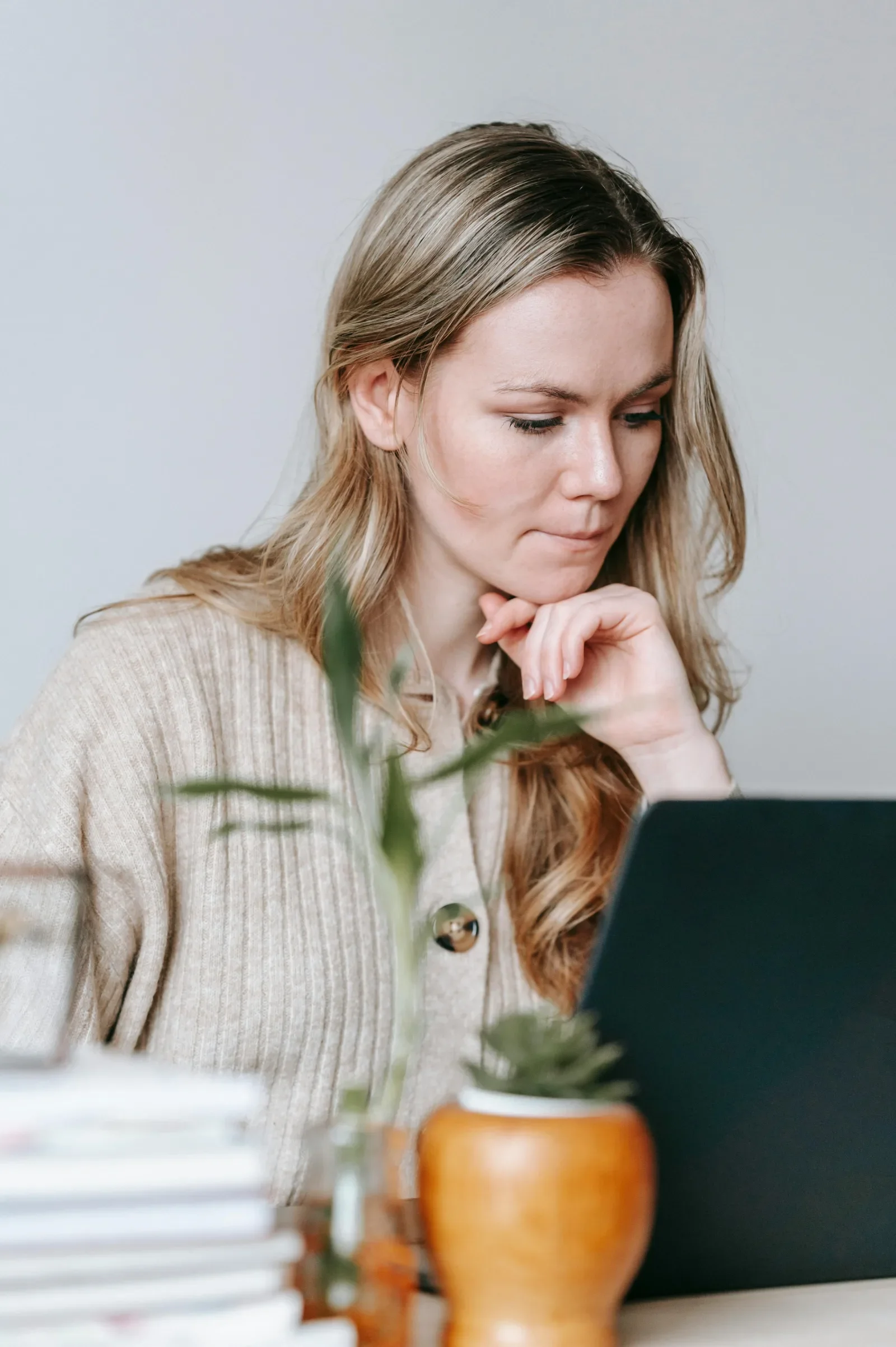 Woman in a beige cardigan looking thoughtfully at her laptop while considering online therapy