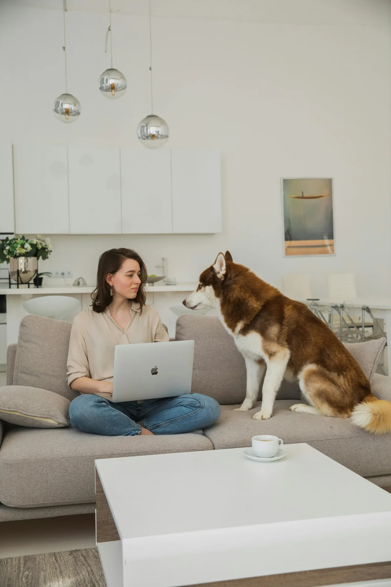 Woman sitting on a couch with her laptop and husky dog during an online therapy session at home