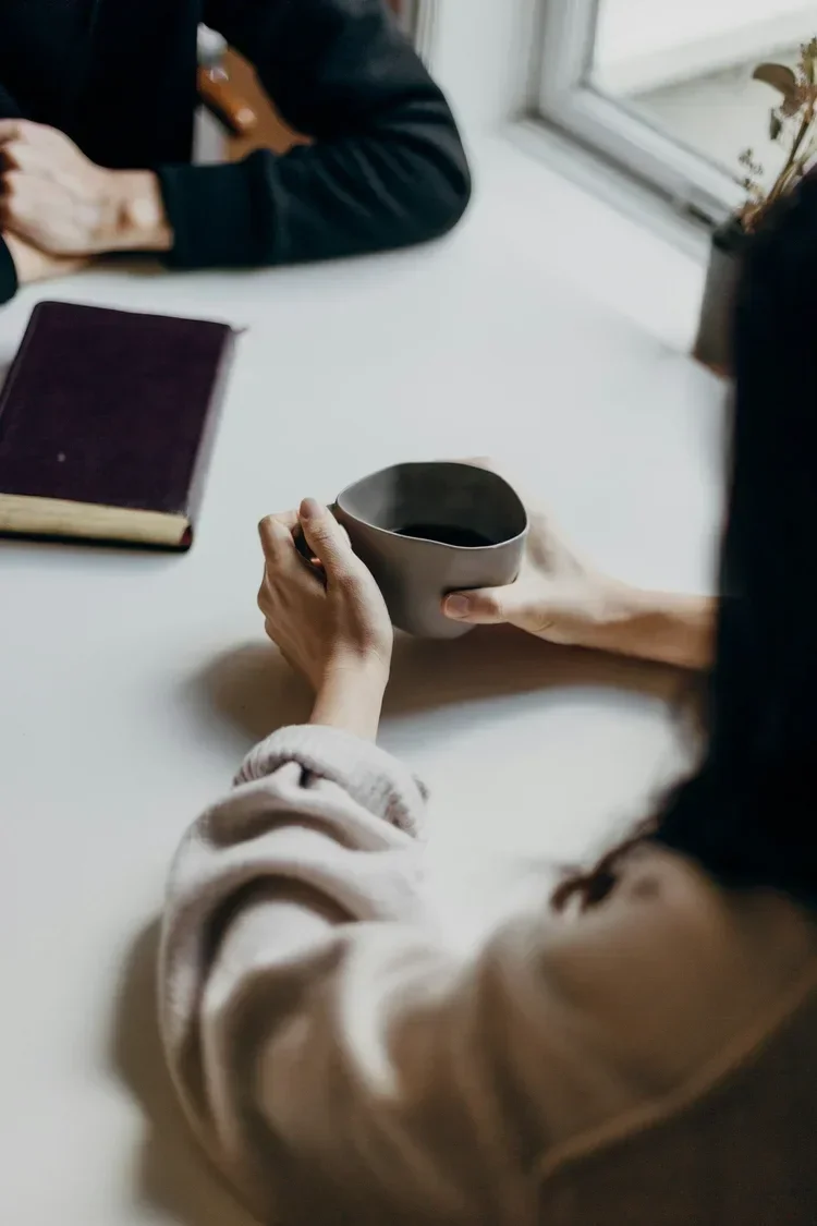 Two people talking over coffee with a Bible on the table, representing supportive faith-based counseling conversations