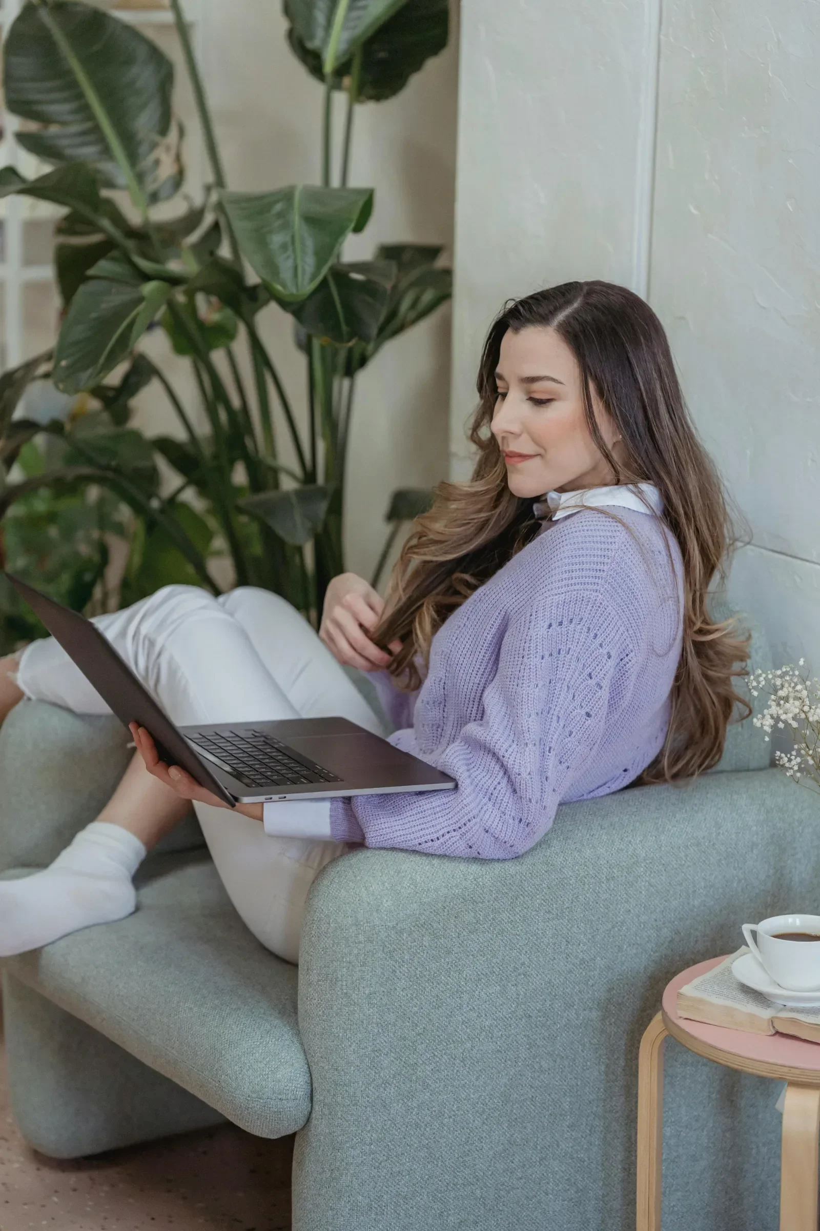 Woman in a lavender sweater using a laptop on a cozy armchair during an online faith-based therapy session