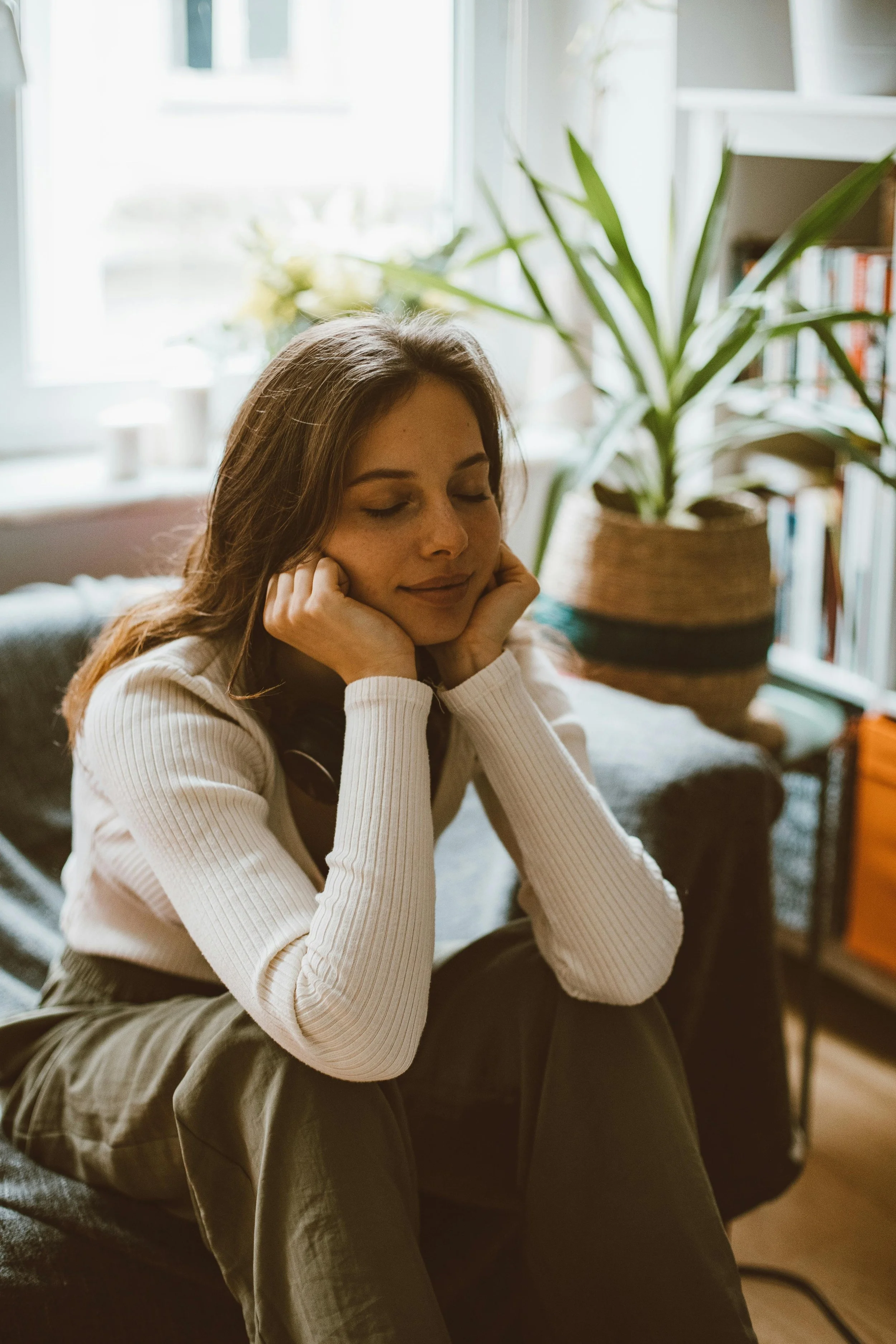 Woman sitting calmly with eyes closed in a cozy home, representing emotional regulation, inner calm, and healing through therapy