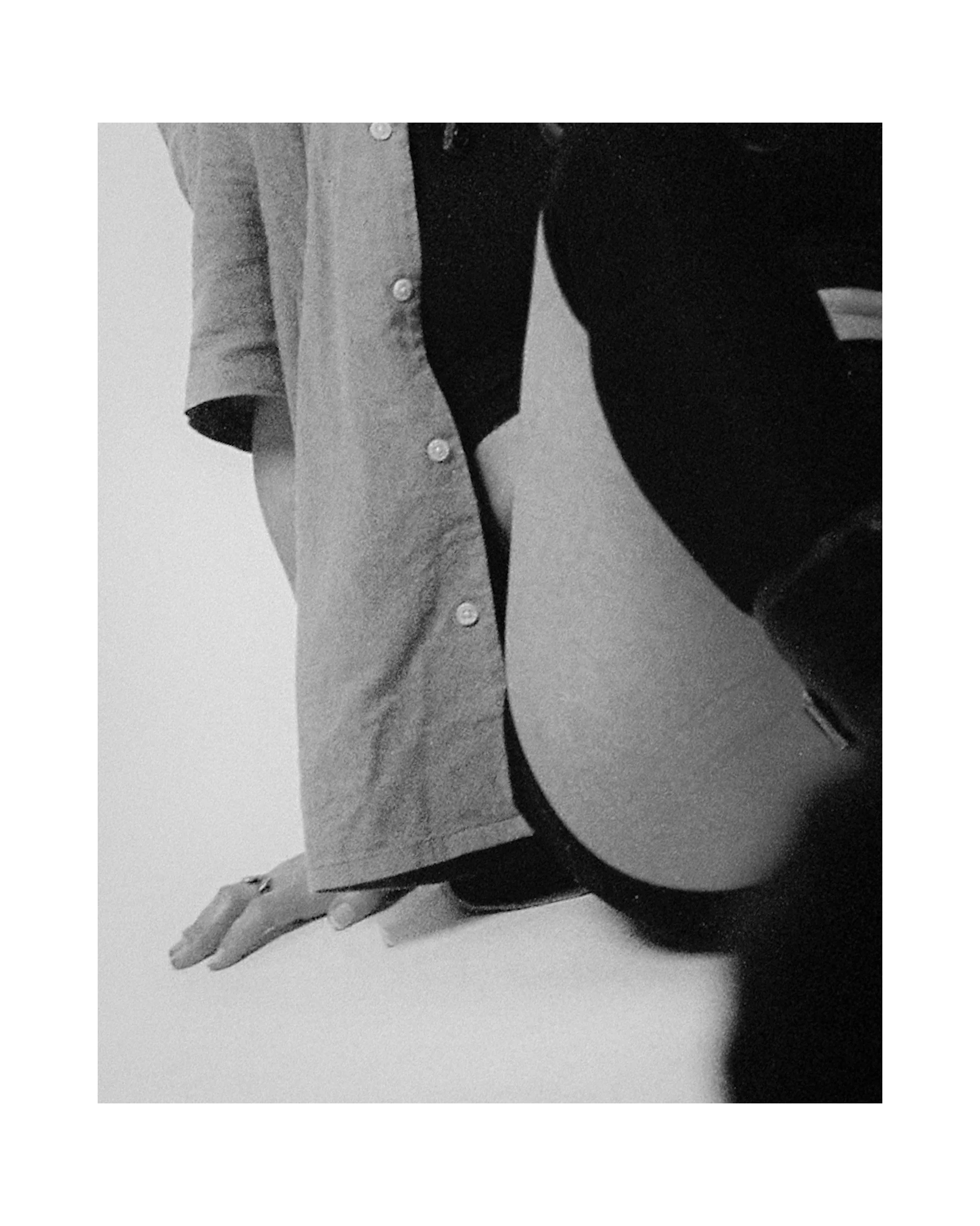 A black-and-white photo showing a person kneeling on a flat surface, wearing a long-sleeve shirt, pants, and knee-high boots, with their hand resting on the surface.