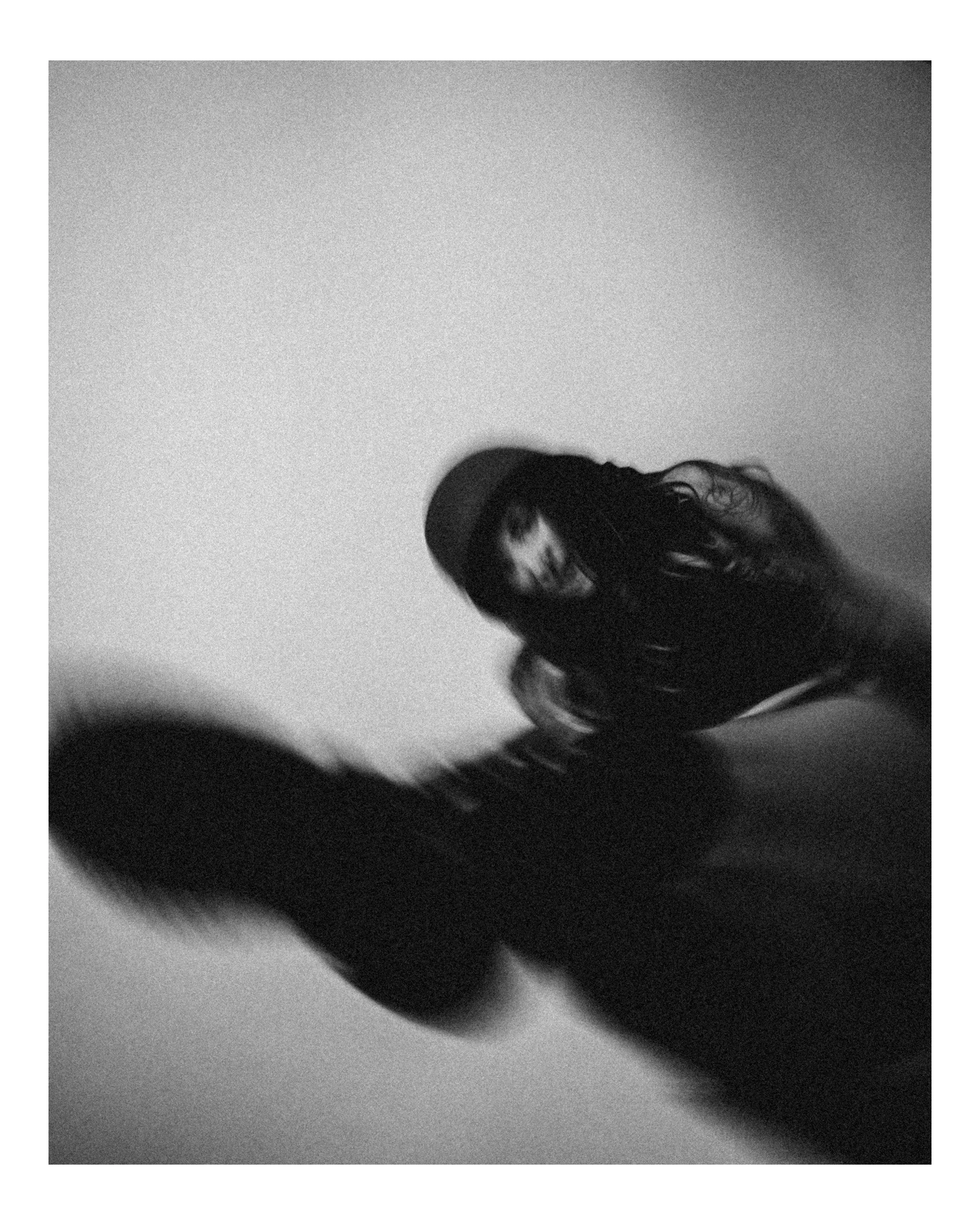 A black and white photo of a woman with long hair, wearing a hat, looking down with a shadow cast on the ceiling.