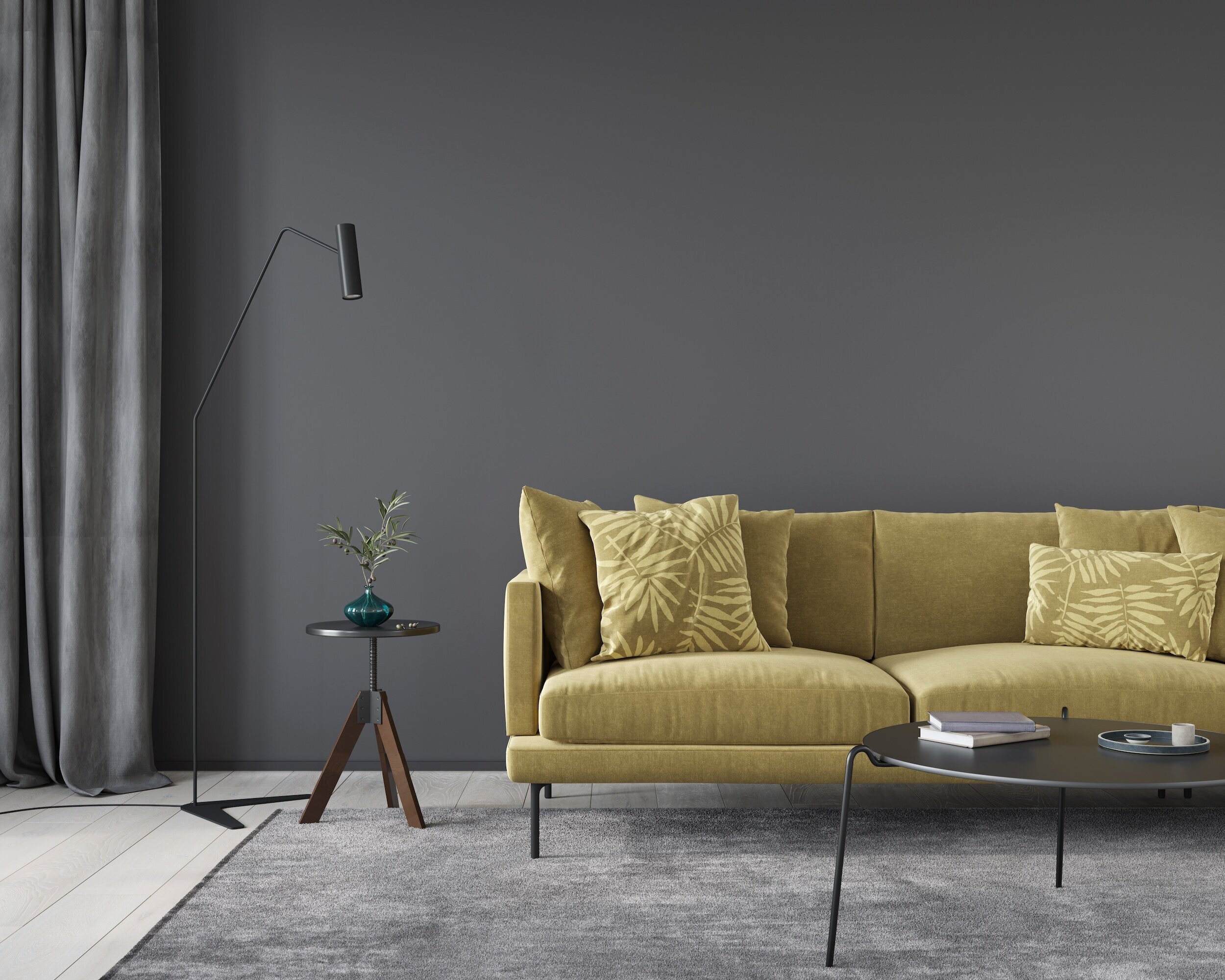 A modern living room with a yellow sofa, matching yellow pillows with leaf patterns, a small black round coffee table with a book and a marble object, a small round side table with a teal vase and plant, a floor lamp with a black shade, gray curtains, a gray wall, and a gray rug.