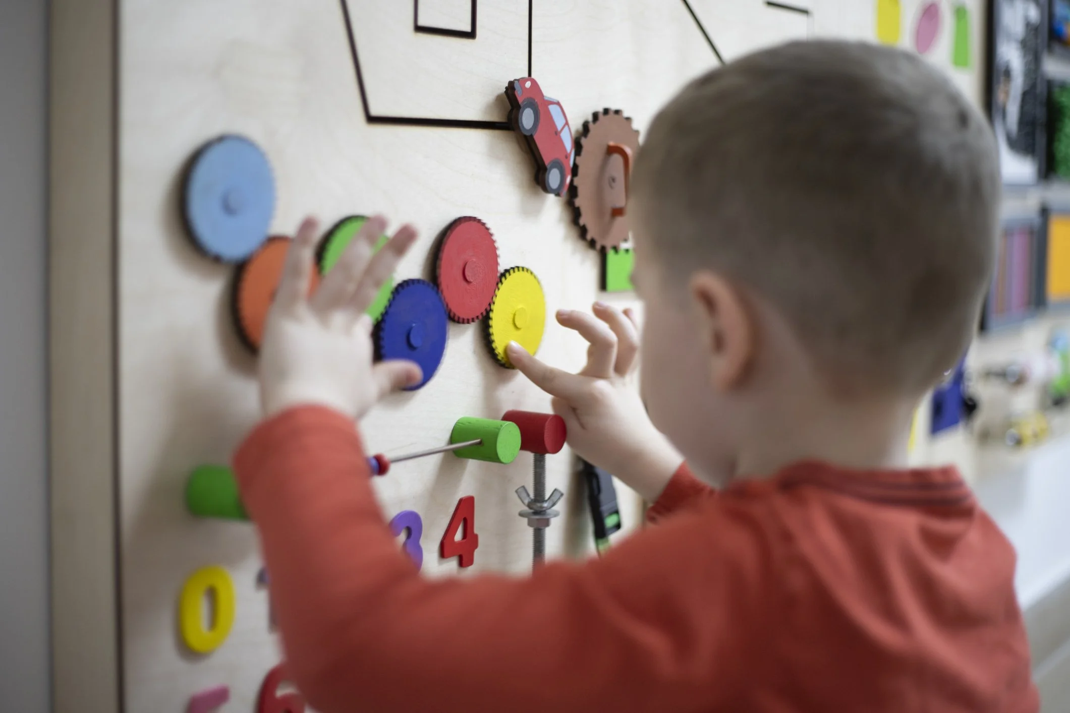 Child placing colorful gear-shaped pieces on a vertical pegboard with numbers.