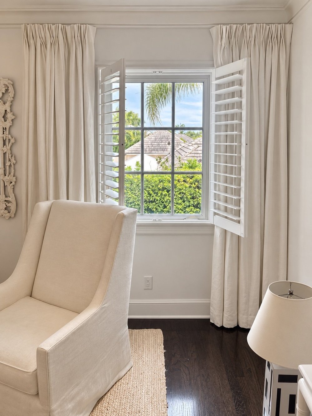 Hinged white shutter panels opened beside a bedroom window with neutral drapery