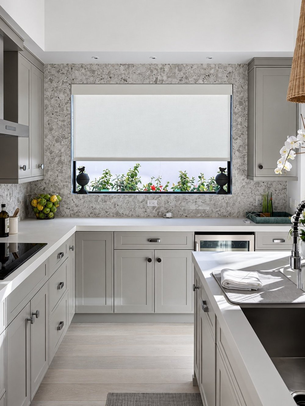 White roller shade above grey kitchen cabinets and a stone backsplash