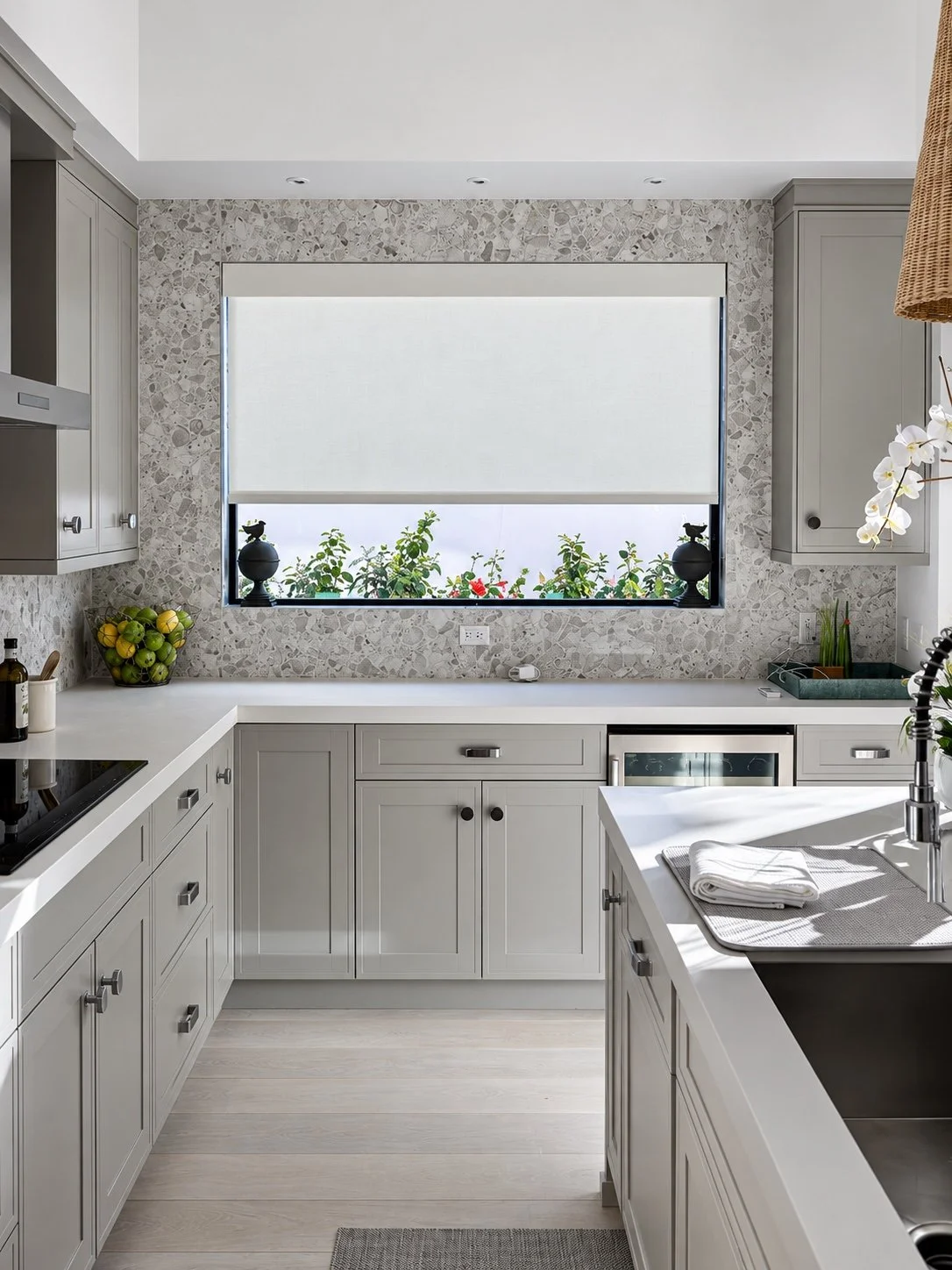 White roller shade above gray kitchen cabinets and a stone backsplash