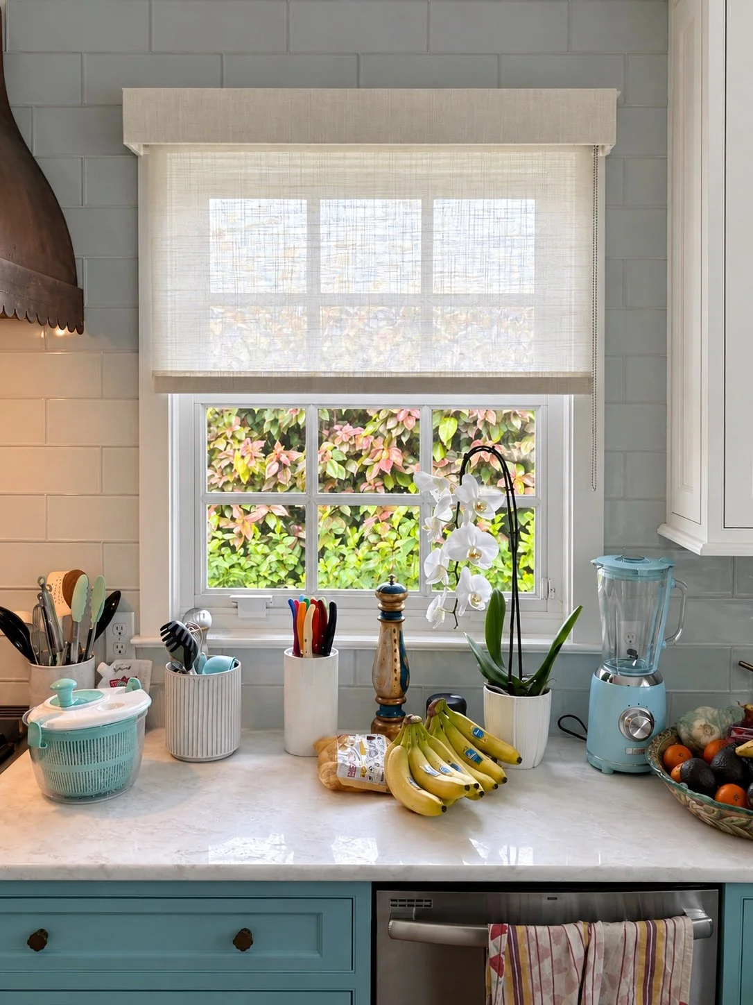 Textured roller shade above a kitchen window and pale blue cabinetry