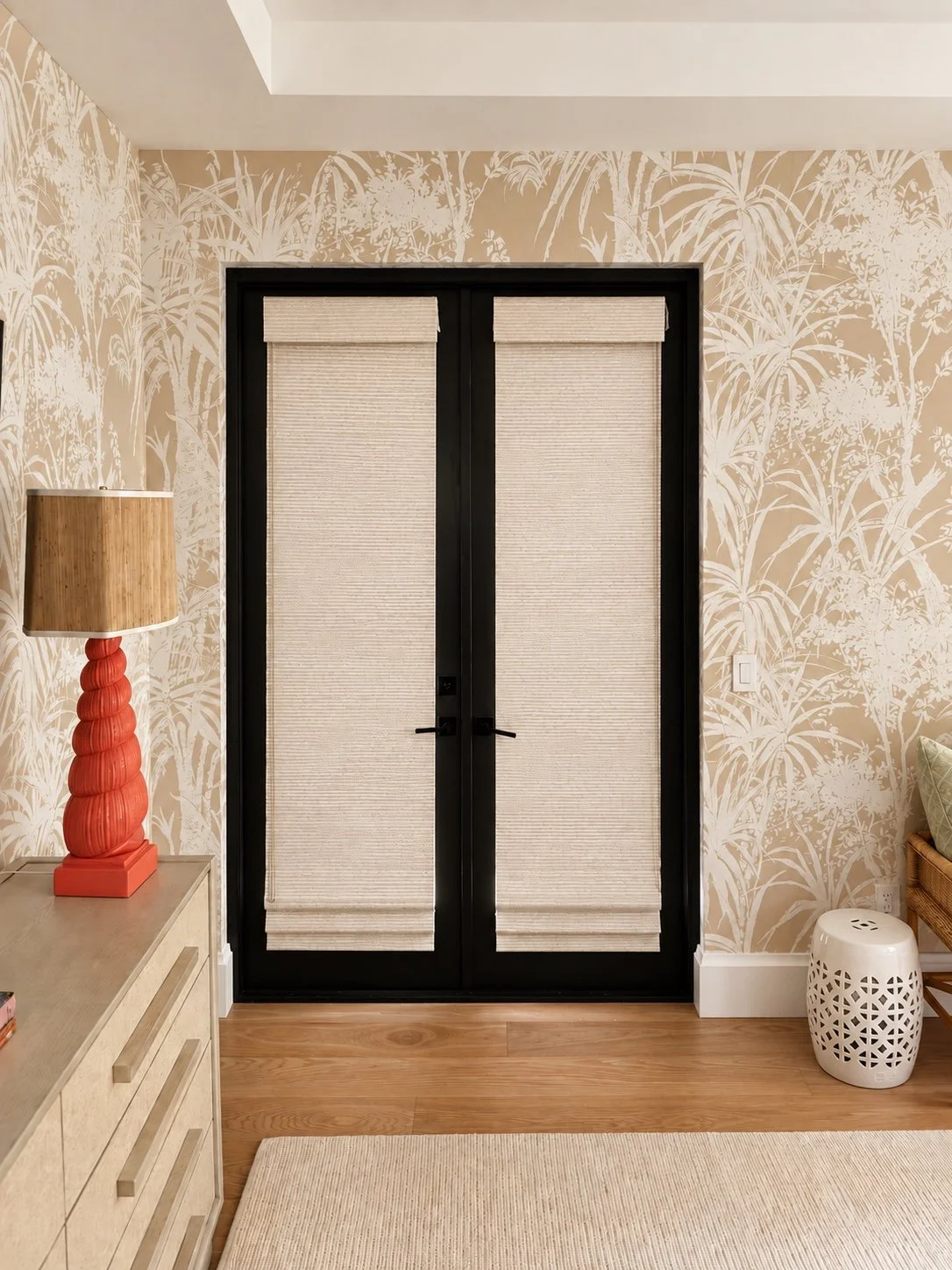 Two woven Roman shades fitted to black French doors against patterned wallpaper