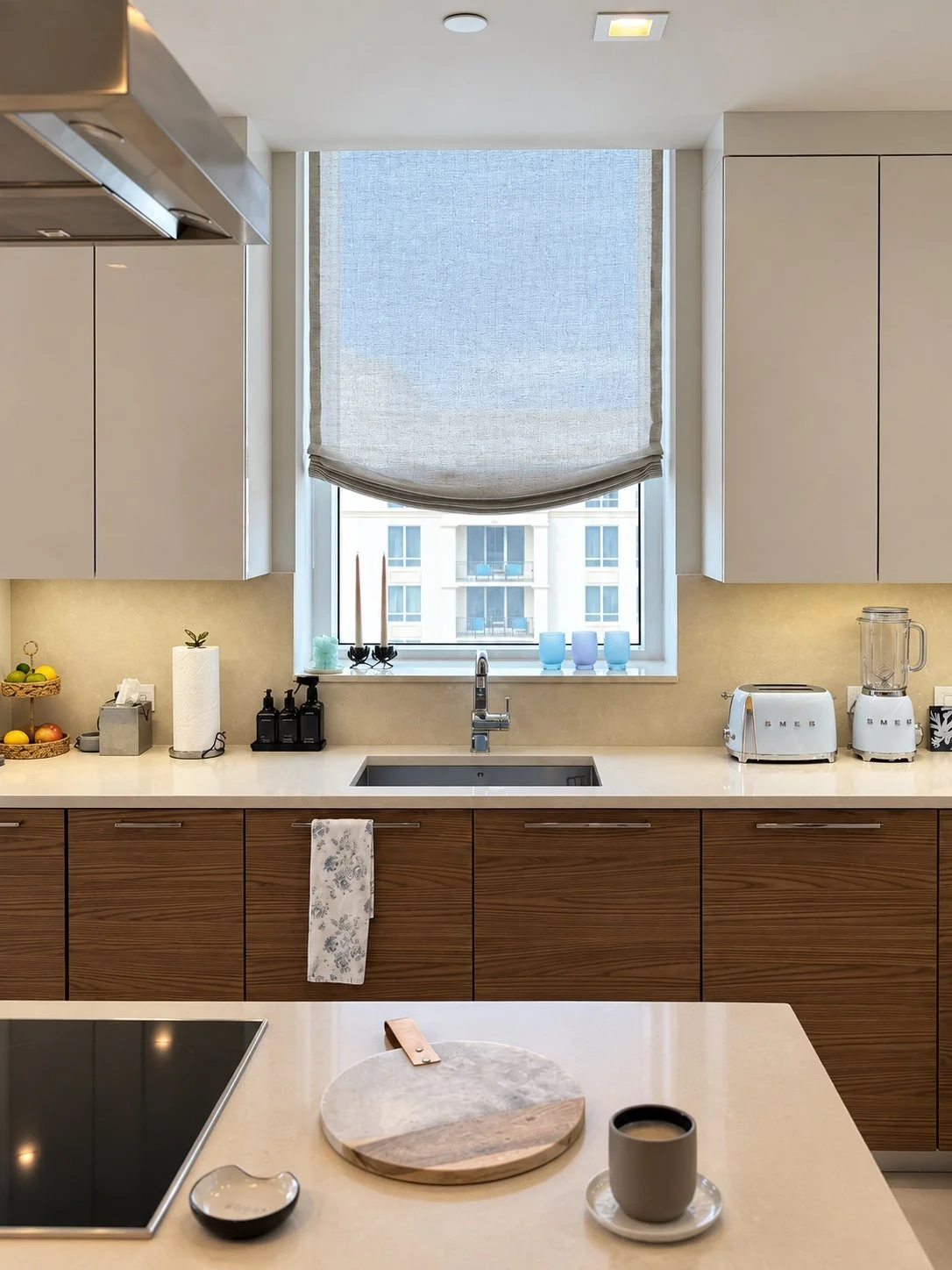 Relaxed fabric Roman shade above a kitchen sink with wood cabinetry