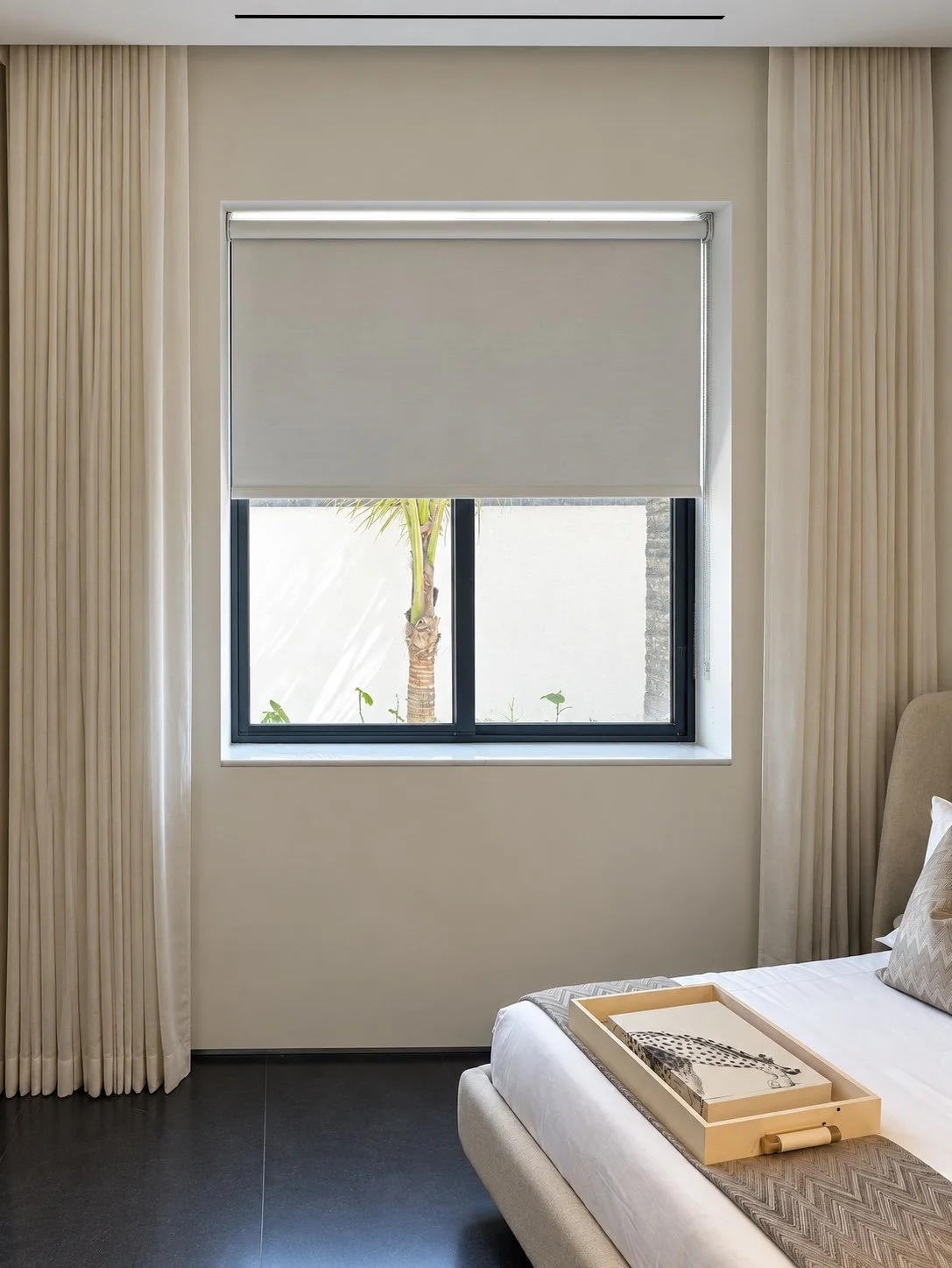 Neutral roller shade layered with full-length cream bedroom drapery