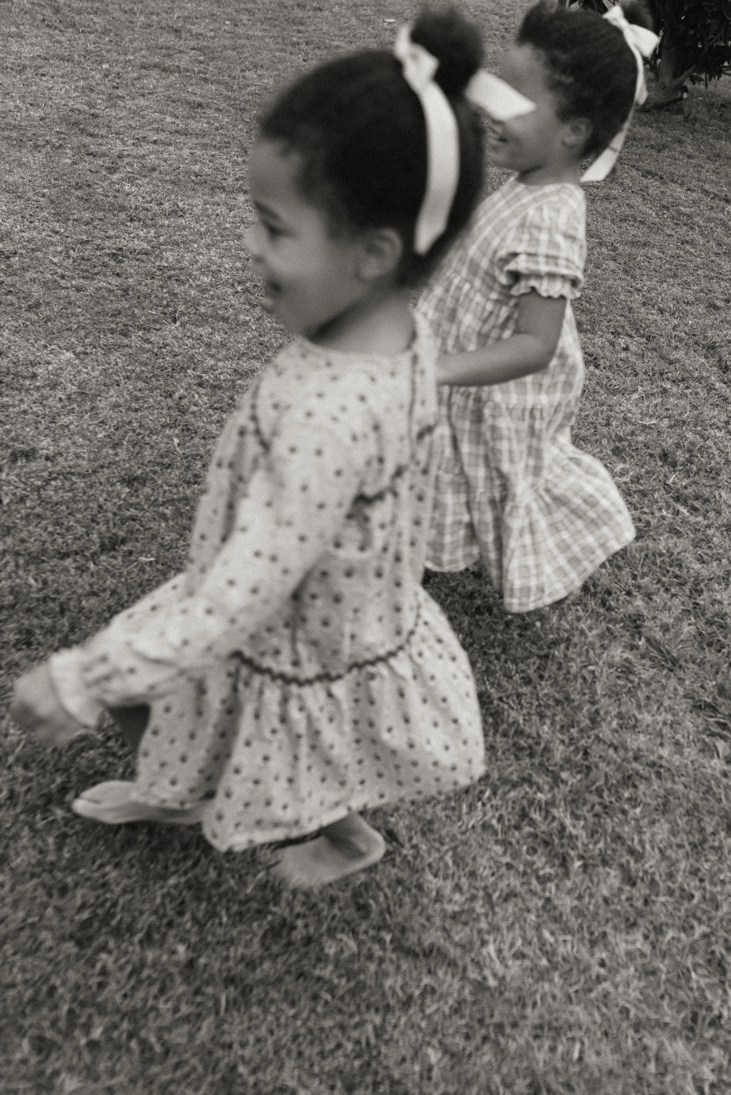 Two young girls with dark hair wearing dresses and headbands, playing together on a grassy field.
