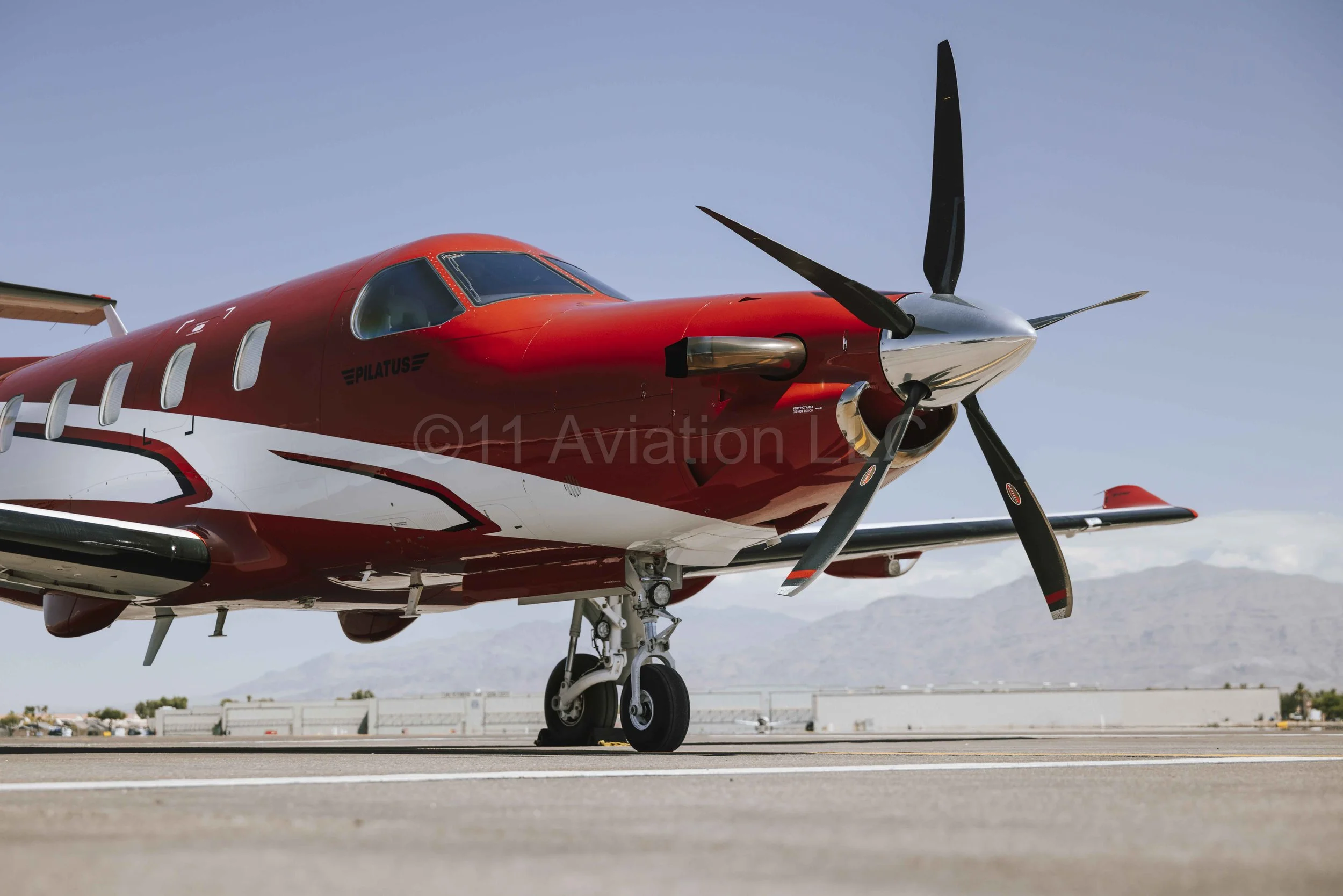 Red and white Pilatus PC12 NGX aircraft parked on tarmac at airport.