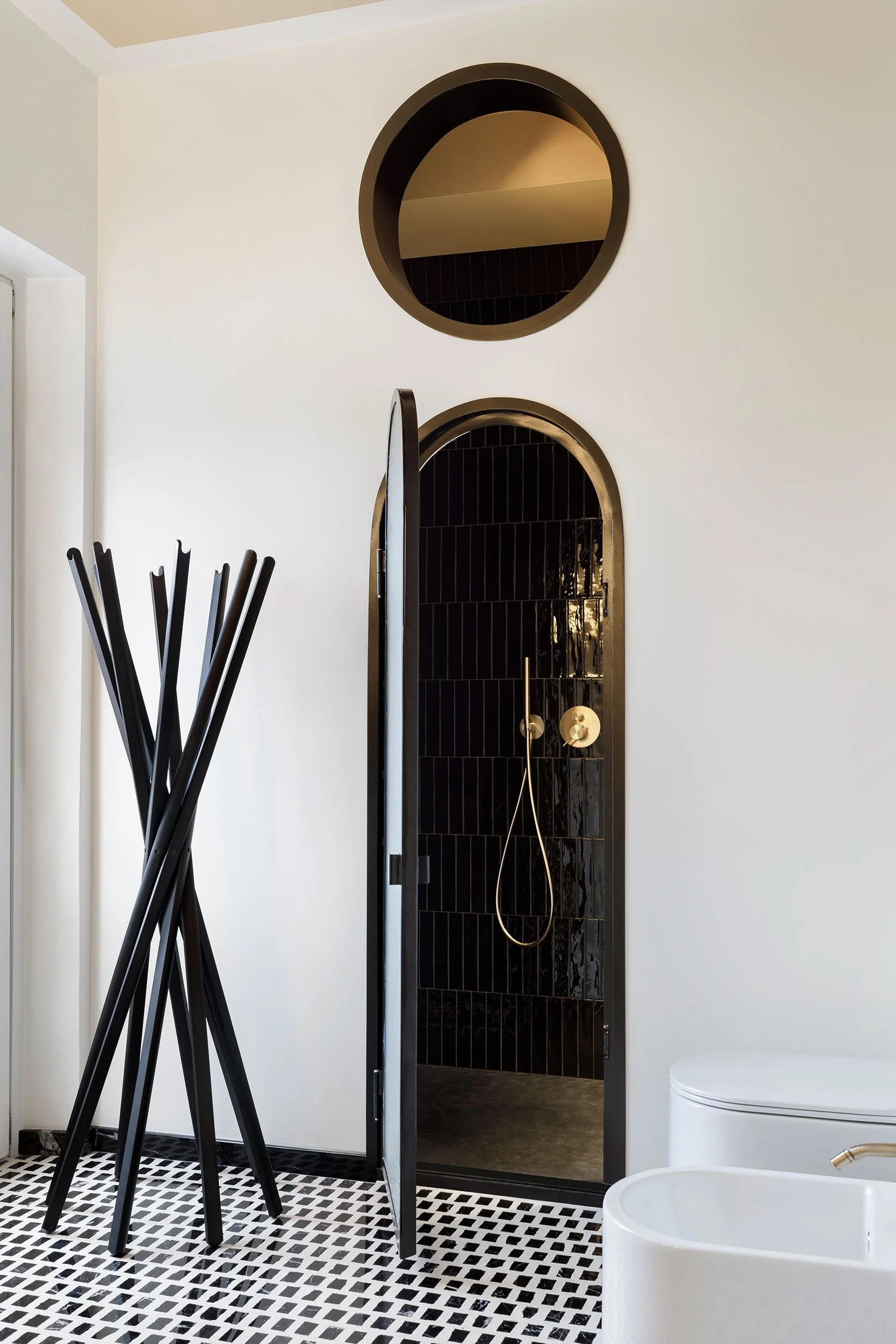 Zona doccia di un bagno moderno in appartamento a Milano con rivestimento in piastrelle nere lucide, apertura ad arco e rubinetteria in finitura oro