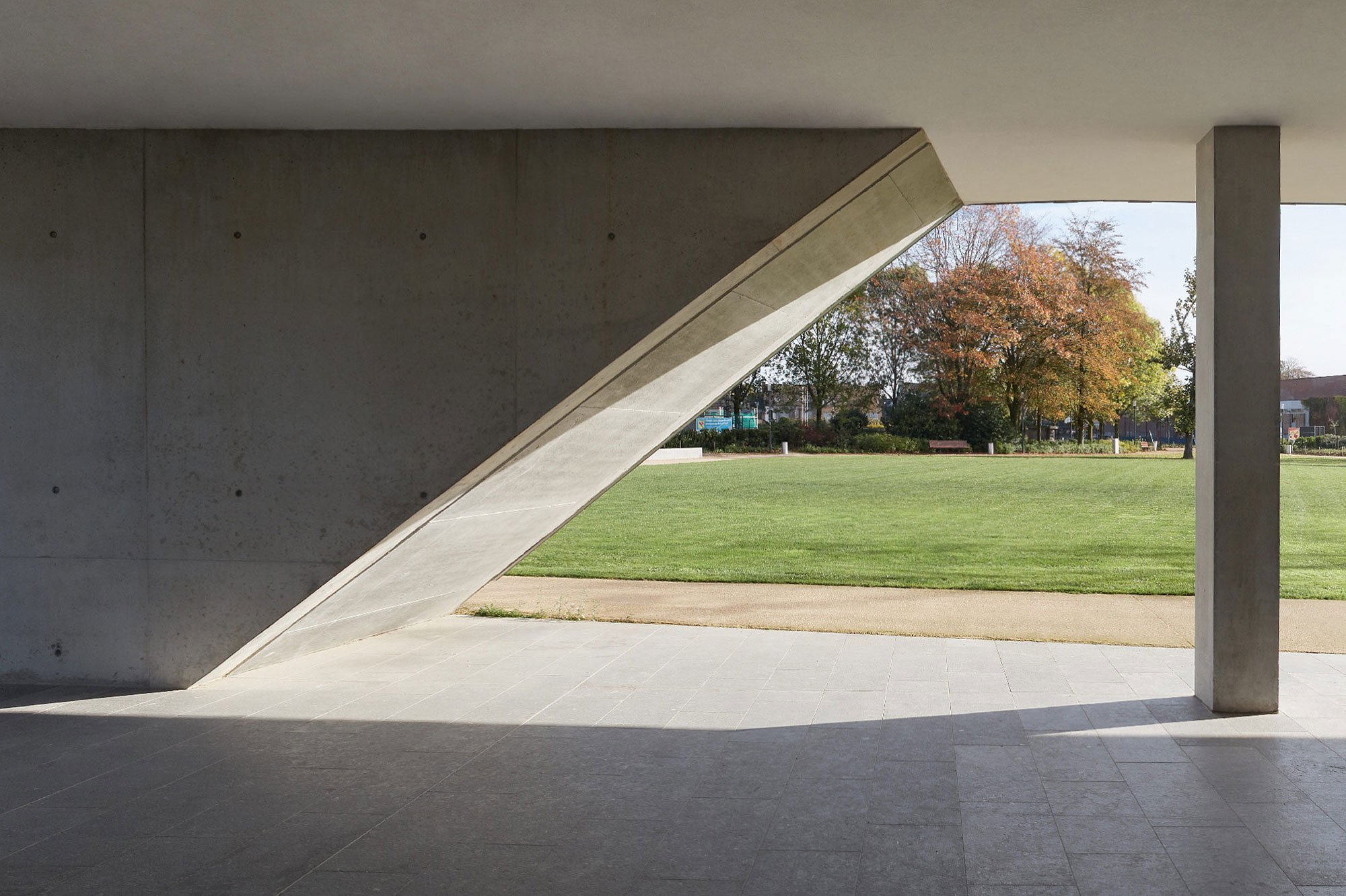 Concrete architectural opening at the Stadskantoor in Torhout, showing an accessible covered passage connecting the public interior with the surrounding green landscape.