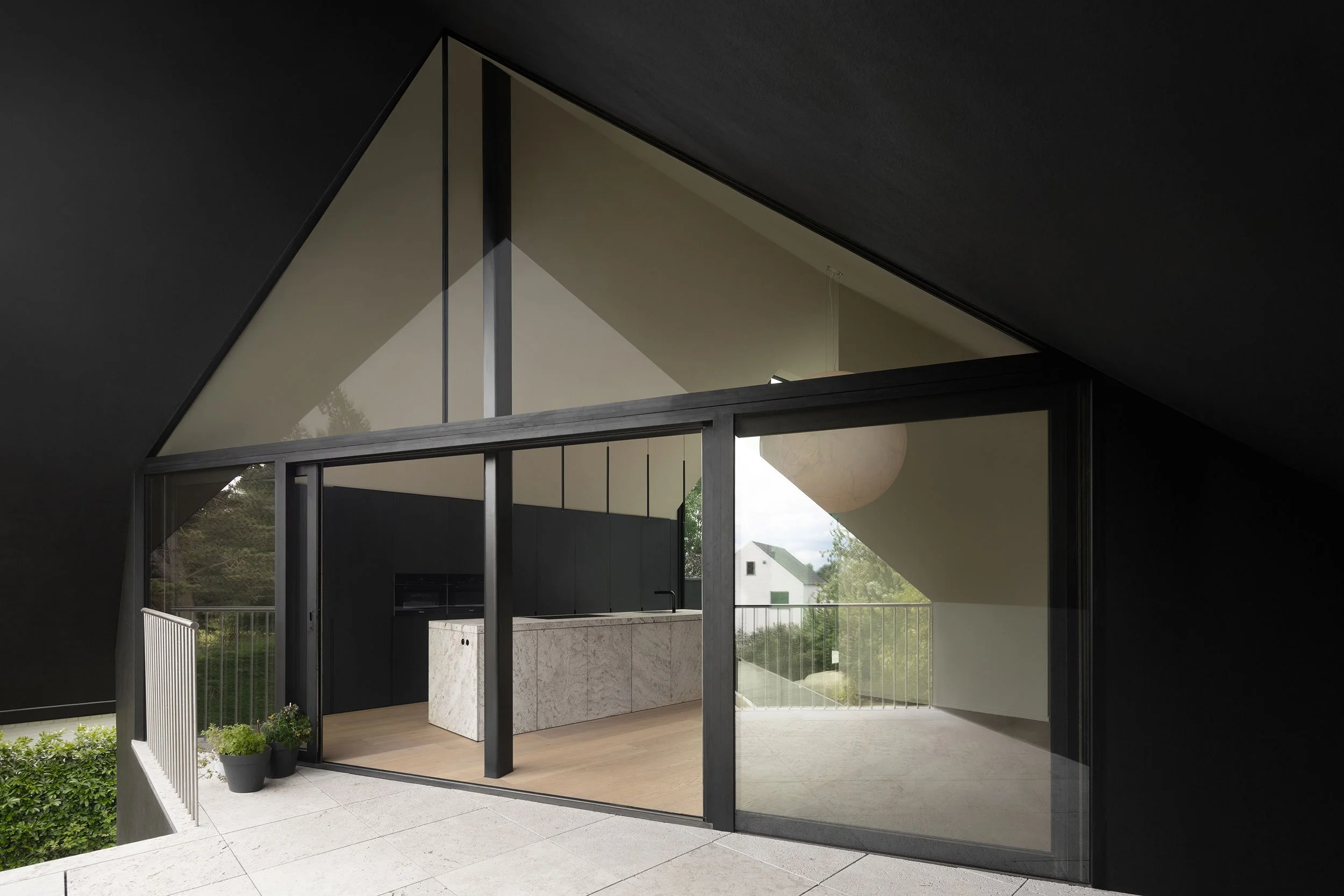 modern residential kitchen with a marble island, large glass façade, and a spherical Moon lamp by Davide Groppi, opening to a terrace surrounded by greenery
