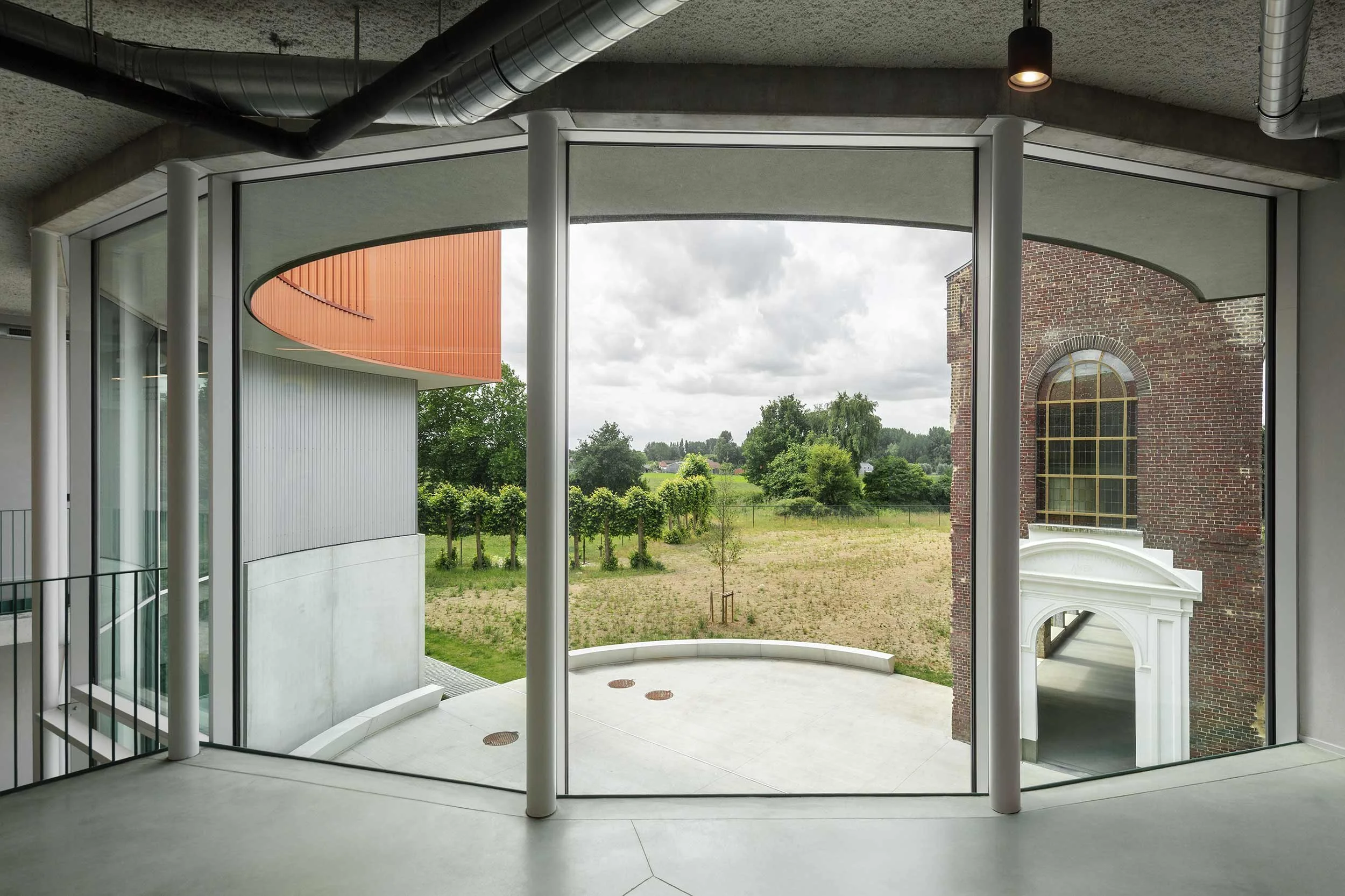 Building of a Multifunctional Center in Knesselare with big windows overlooking the countryside and the preserved convent chapel alongside the modern orange and gray facade.