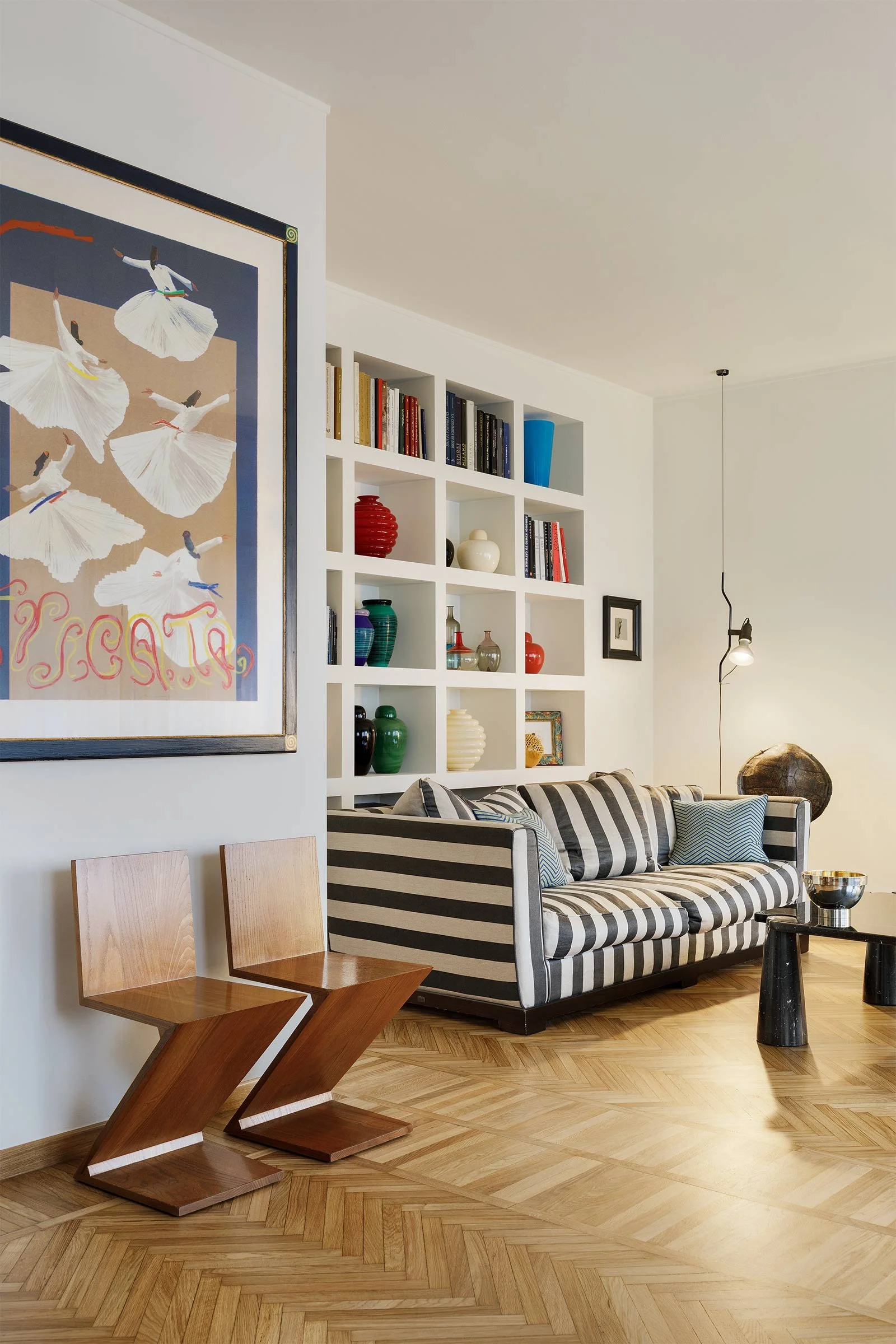 Fotografia d’interni di un soggiorno di un appartamento a Milano, caratterizzato da una libreria in muratura su misura, divano a righe in tessuto, una selezione di arredi e oggetti decorativi, con sedie di Cassina e lampada Flos.