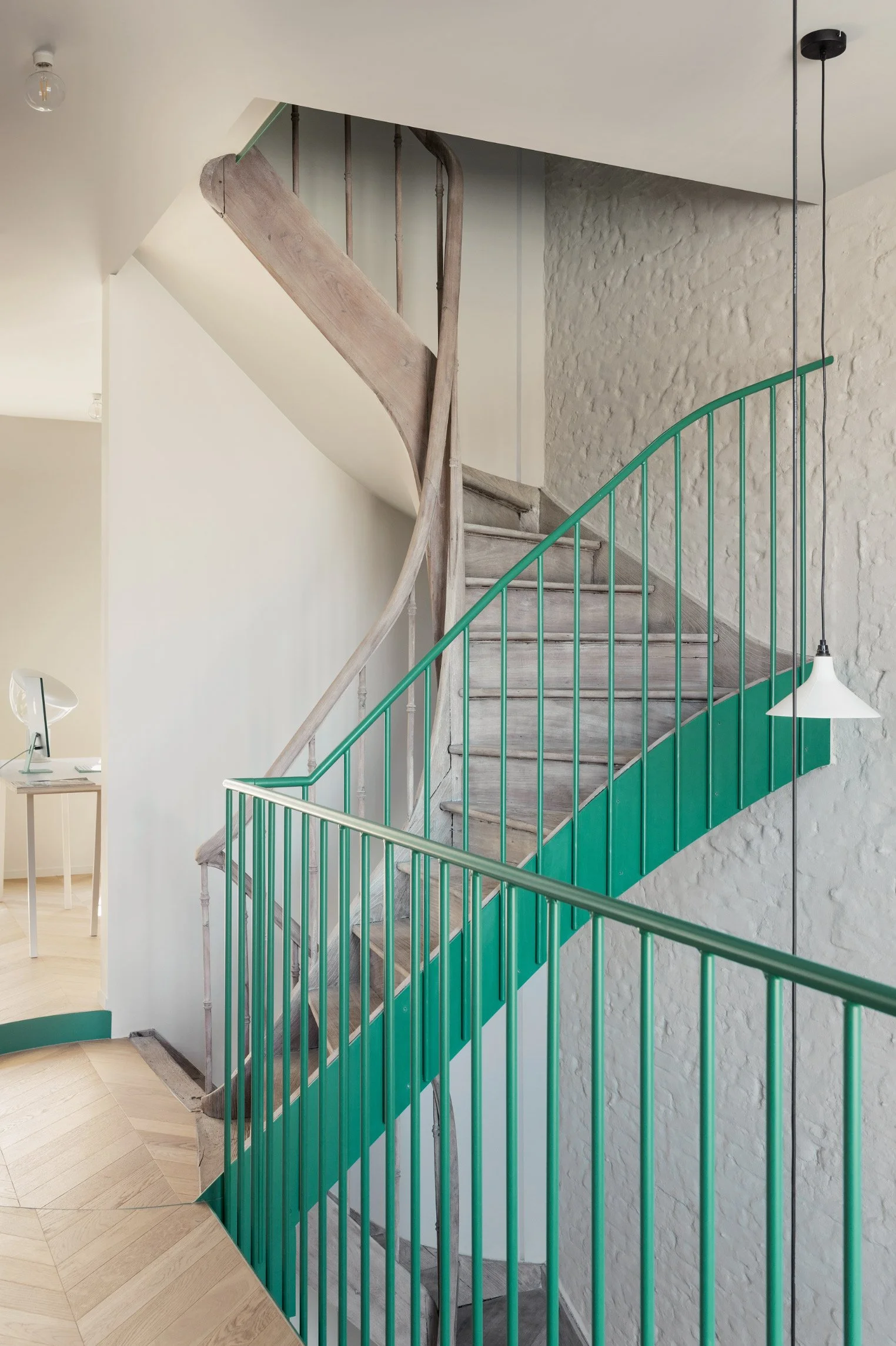 Detail of a restored wooden staircase with a green railing and a Serax Seam lamp in a renovated apartment in Bruges.