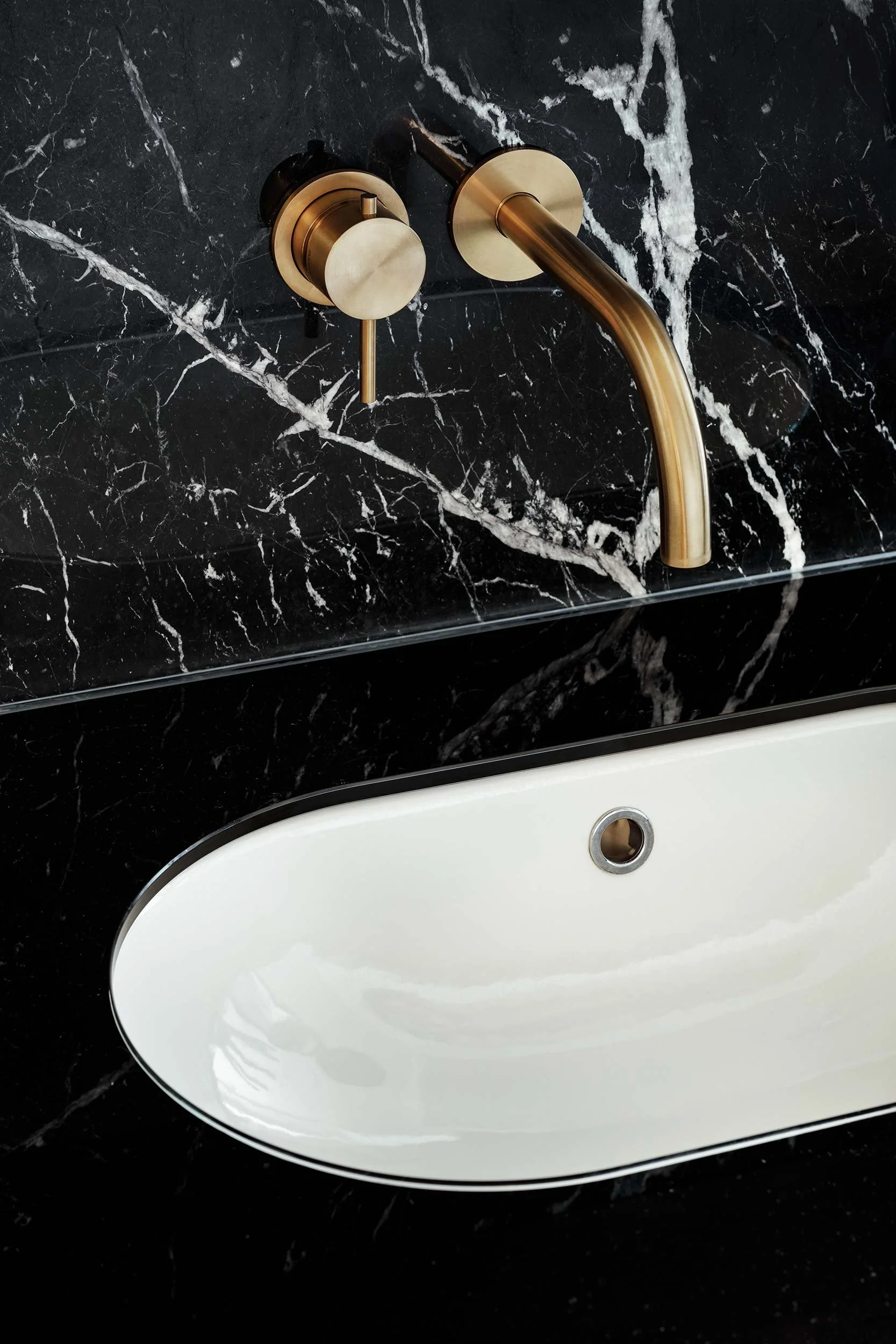Dettaglio di bagno di design in appartamento a Milano con marmo nero venato, lavabo bianco e rubinetteria a parete in ottone satinato