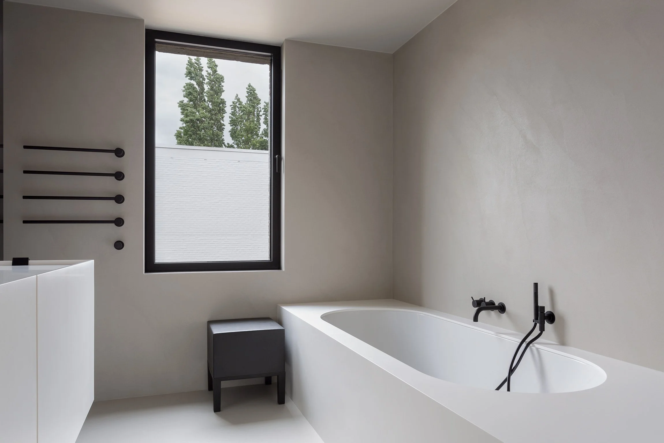 Minimalist bathroom in a private home featuring microcement walls, white ceramic bathtub and Vola matt black fixtures.