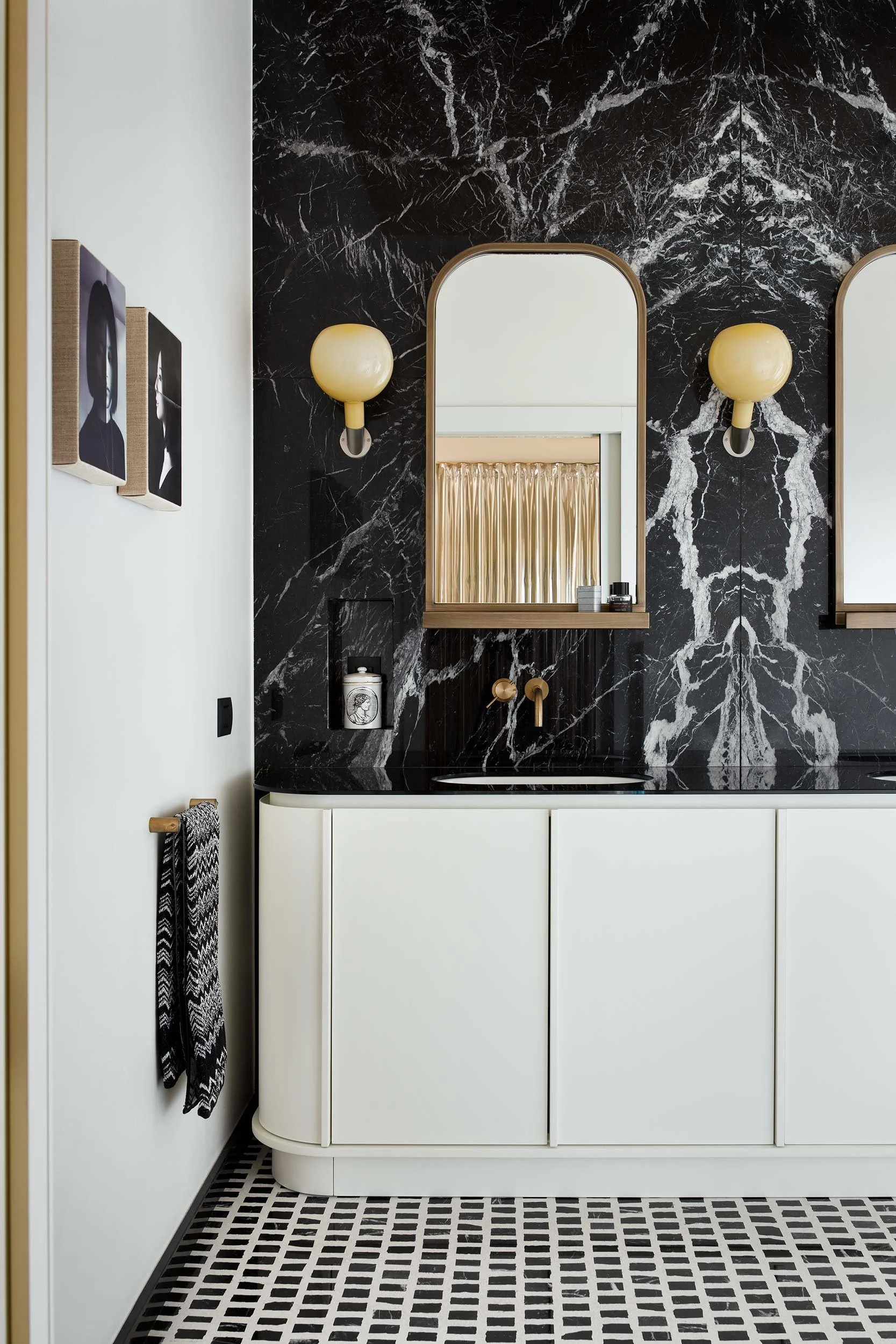 Dettaglio del bagno di un appartamento di design a Milano con mobile lavabo curvo bianco, top scuro e scenografica parete in marmo nero venato